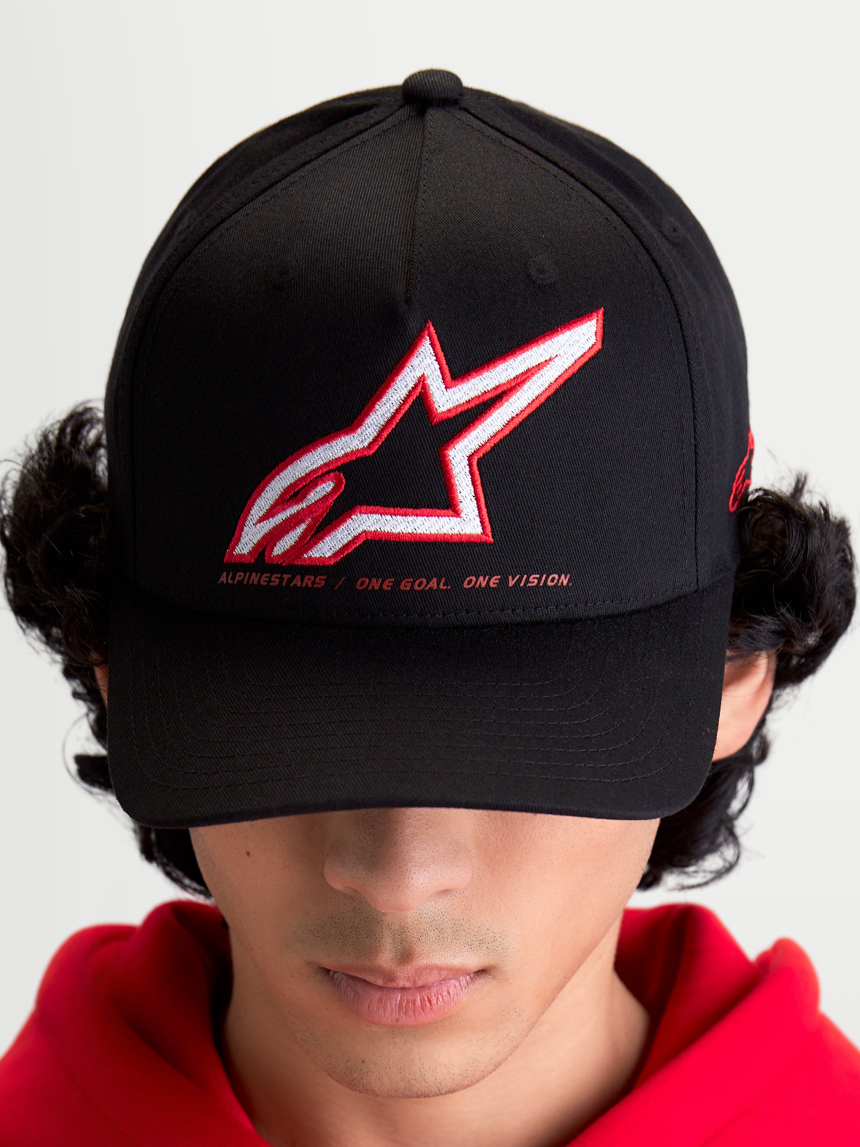 Alpinestars Lineout keps på modell, sportswear baseballkeps för herrar och damer, svart med röd och vit broderad Astars-logotyp och sloganen One Goal One Vision, böjd skärm, strukturerad krona