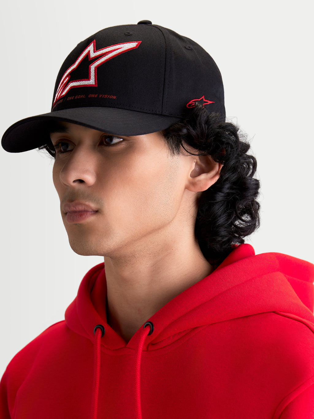 Alpinestars Lineout keps, svart baseballkeps med böjd skärm, strukturerad krona med broderad Astars-logotyp i rött och vitt samt märkning på sidan, visas på en modell.