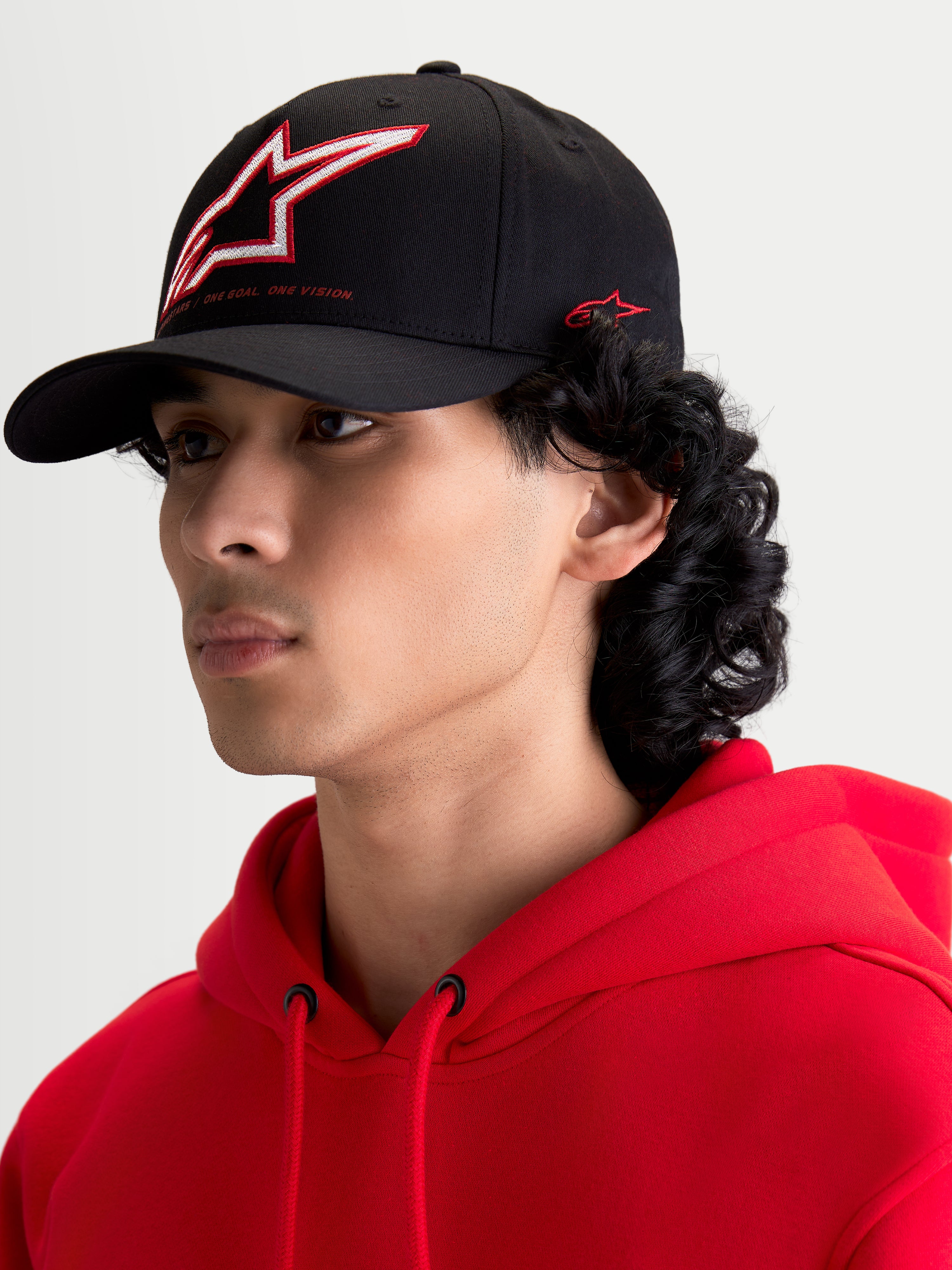 Alpinestars Lineout keps, svart baseballkeps med böjd skärm, strukturerad krona med broderad Astars-logotyp i rött och vitt samt märkning på sidan, visas på en modell.