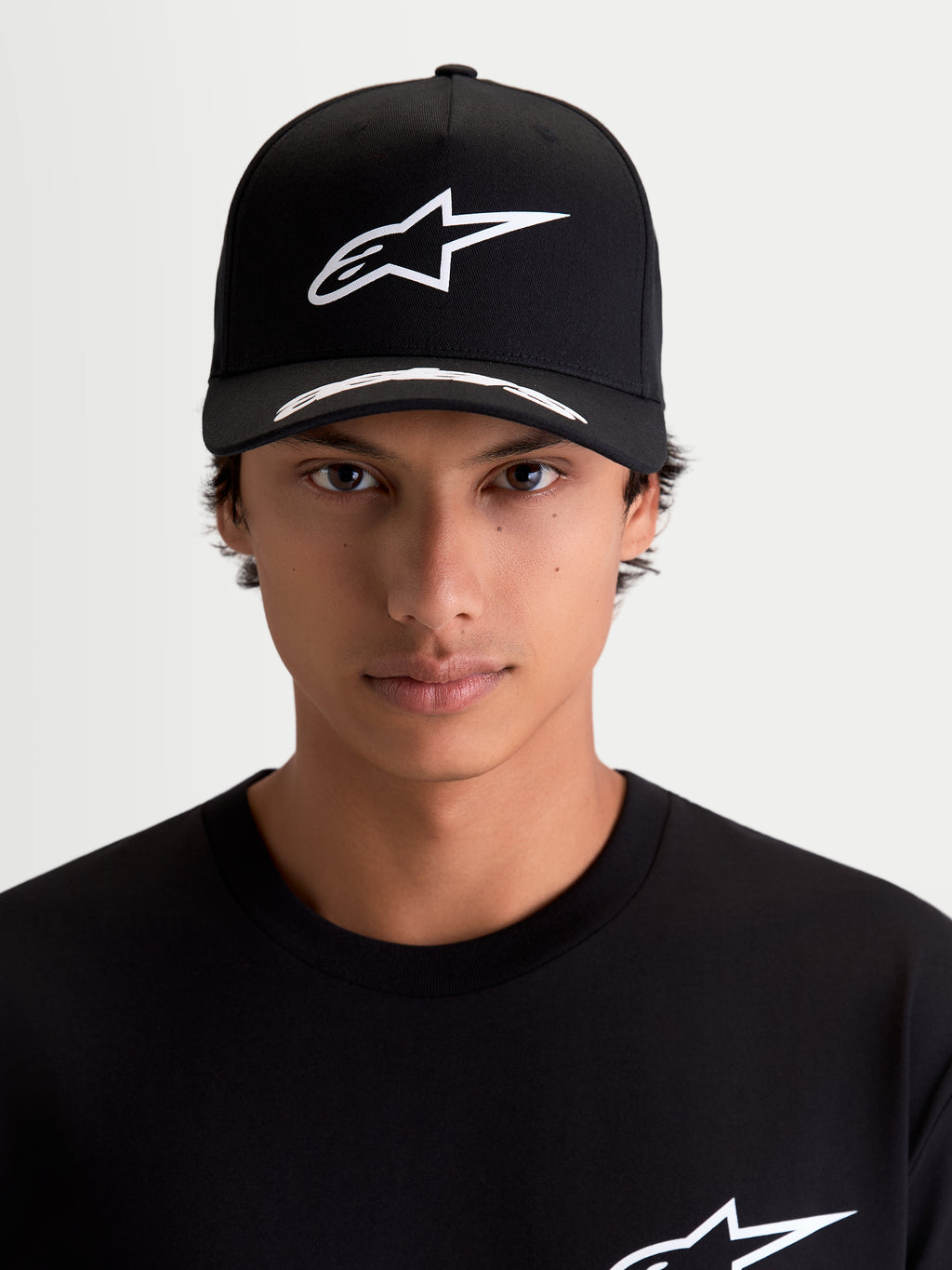 Alpinestars Arclight keps, motorsportkeps, svart och vit, vit pufftryckt Astars-logotyp på strukturerad krona, böjd skärm med logodetaljer, premium twill, frontvy på modell.
