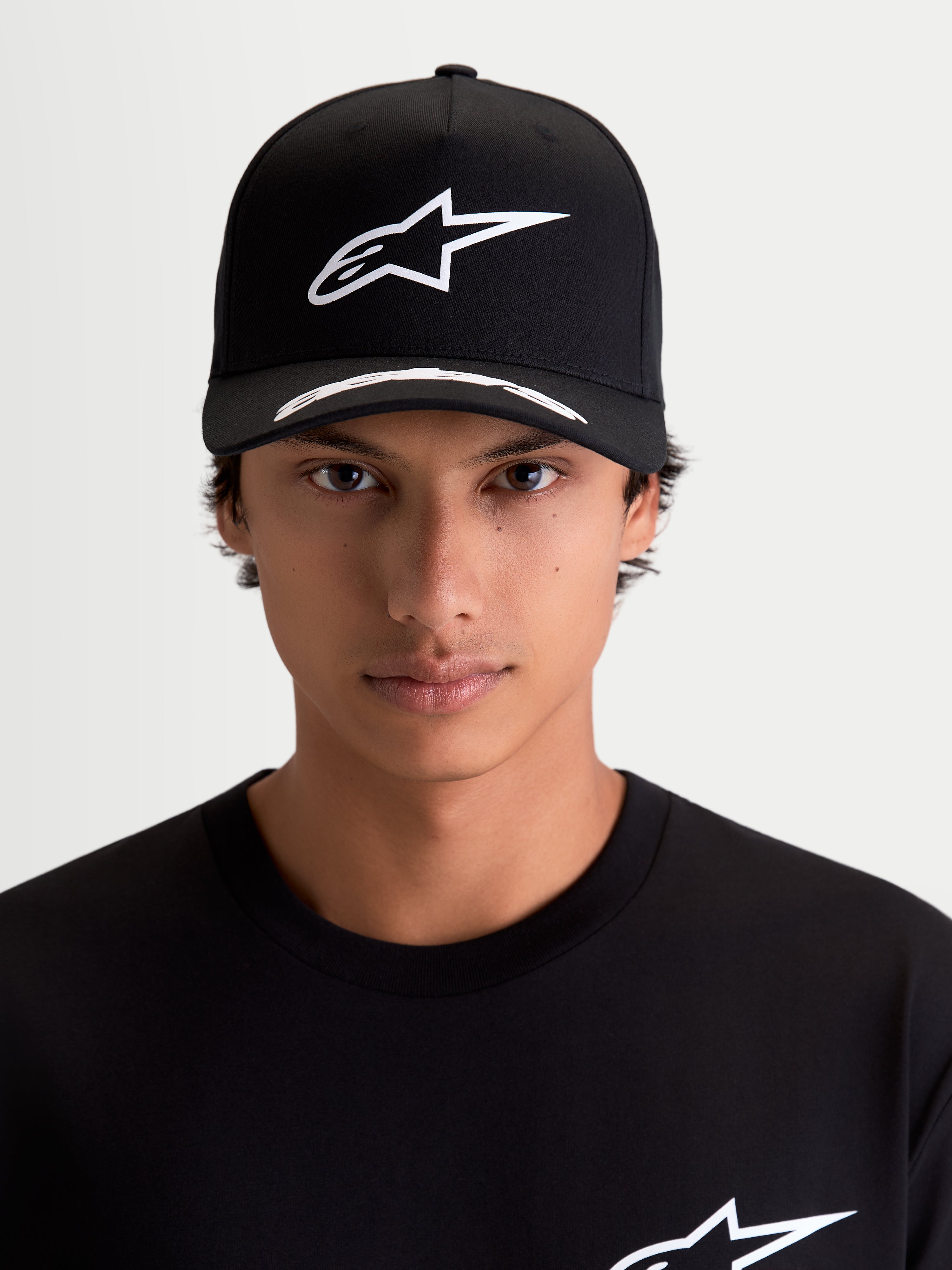 Alpinestars Arclight keps, motorsportkeps, svart och vit, vit pufftryckt Astars-logotyp på strukturerad krona, böjd skärm med logodetaljer, premium twill, frontvy på modell.