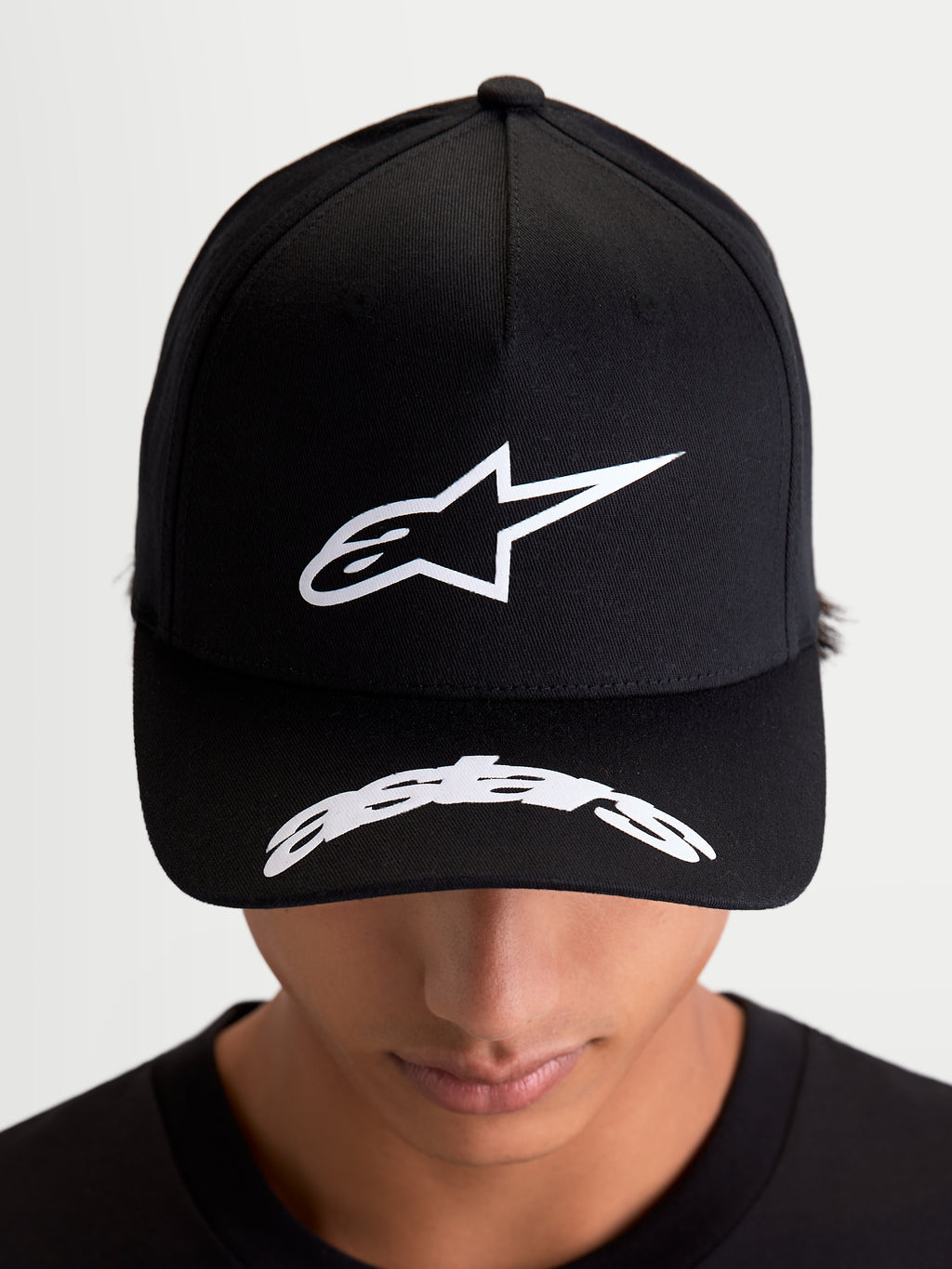 Alpinestars Arclight keps, svart sportkeps med vit texturerad Astars-logotyp i pufftryck, strukturerad krona och vit logotyp på den böjda skärmen, på modell sett framifrån, motorsport-inspirerad vardagsstil
