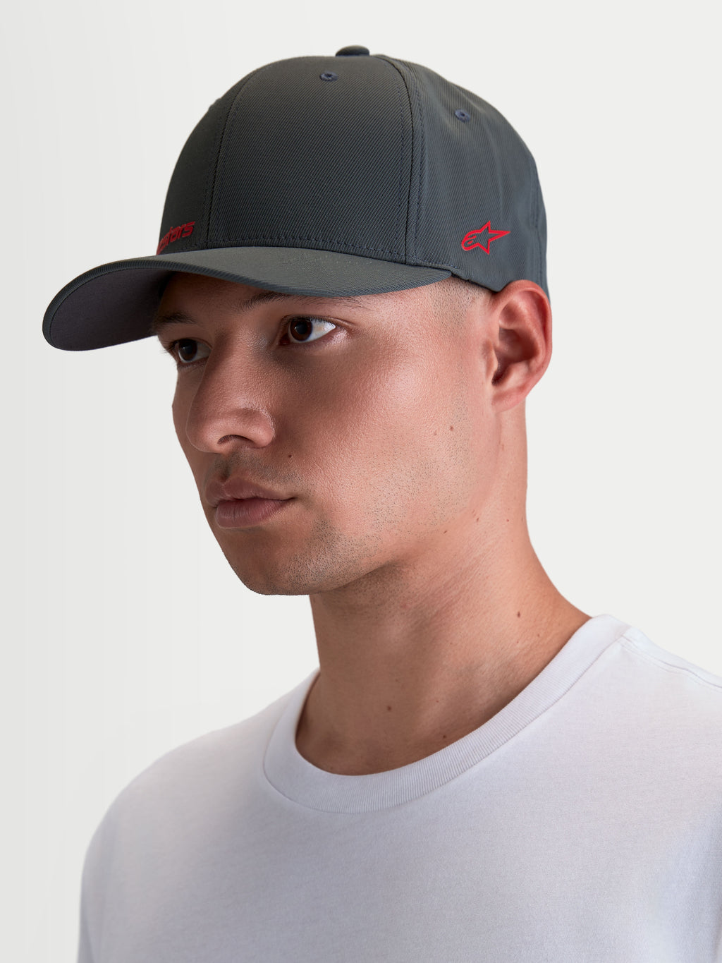 Alpinestars Points keps på modell, mörkgrå sportkeps med böjd skärm och röda logotyper, tillverkad i lätt nylon tactel med flex-back-passform för vardagsbruk.