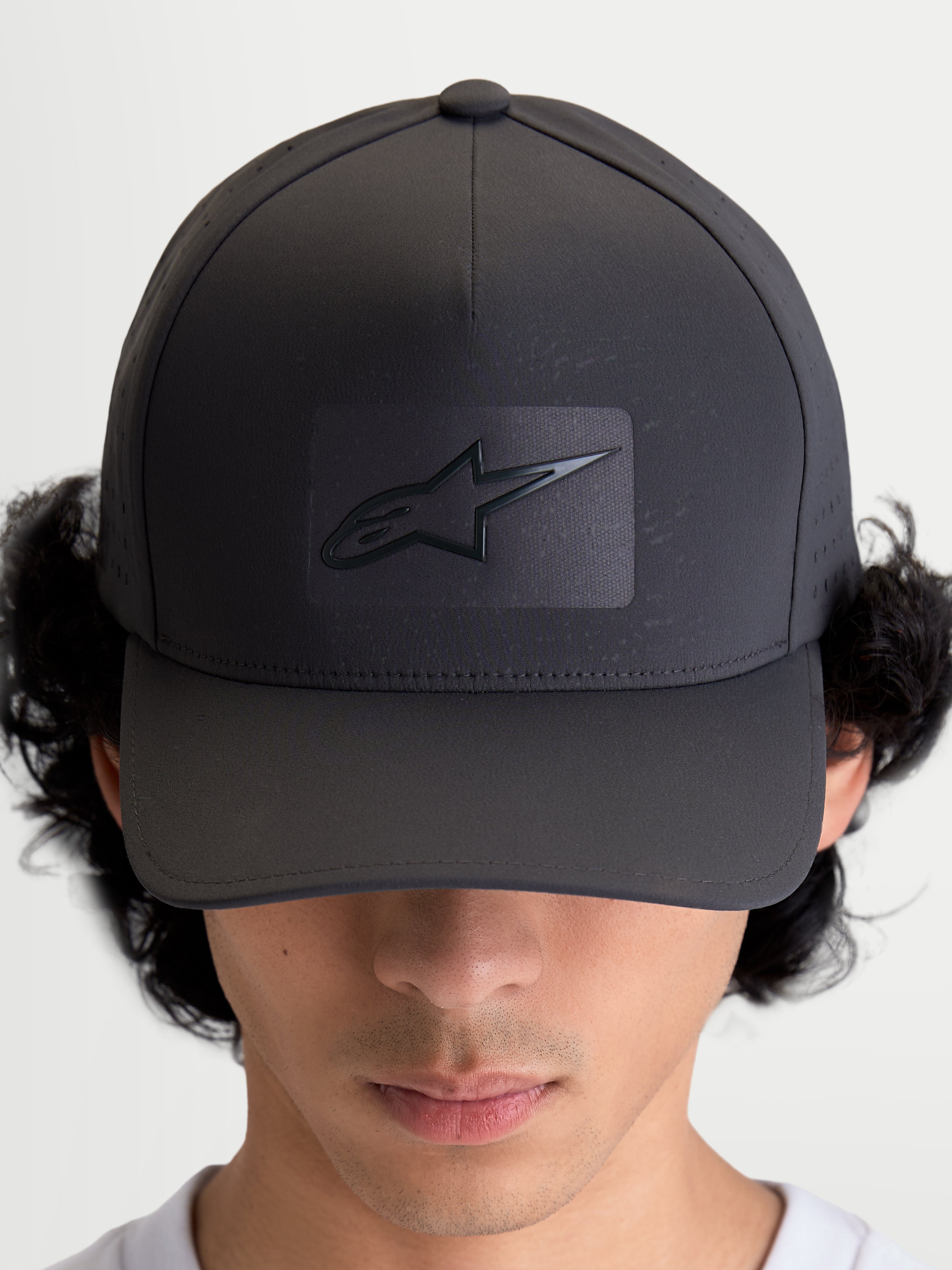 Alpinestars Algo Perf Adjustable keps, mörkgrå sportkeps för vardagsbruk med böjd skärm, strukturerad krona och sonic-weldad Astars-logotyp, sidoperforeringar för luftflöde, sedd framifrån på modell.