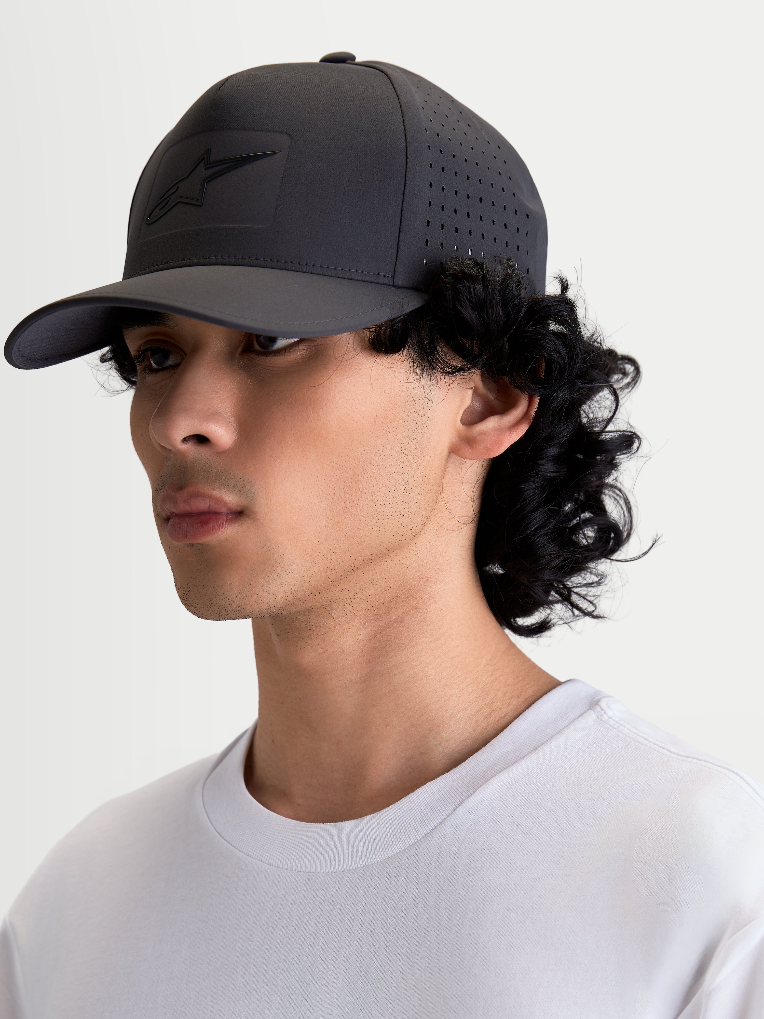 Alpinestars Algo Perf Adjustable keps, mörkgrå sportswear-snapback på modell i sidovy, visar sidoperforeringar för luftflöde, tekniskt tyg, sonic-weld-logotyp och böjd skärm.