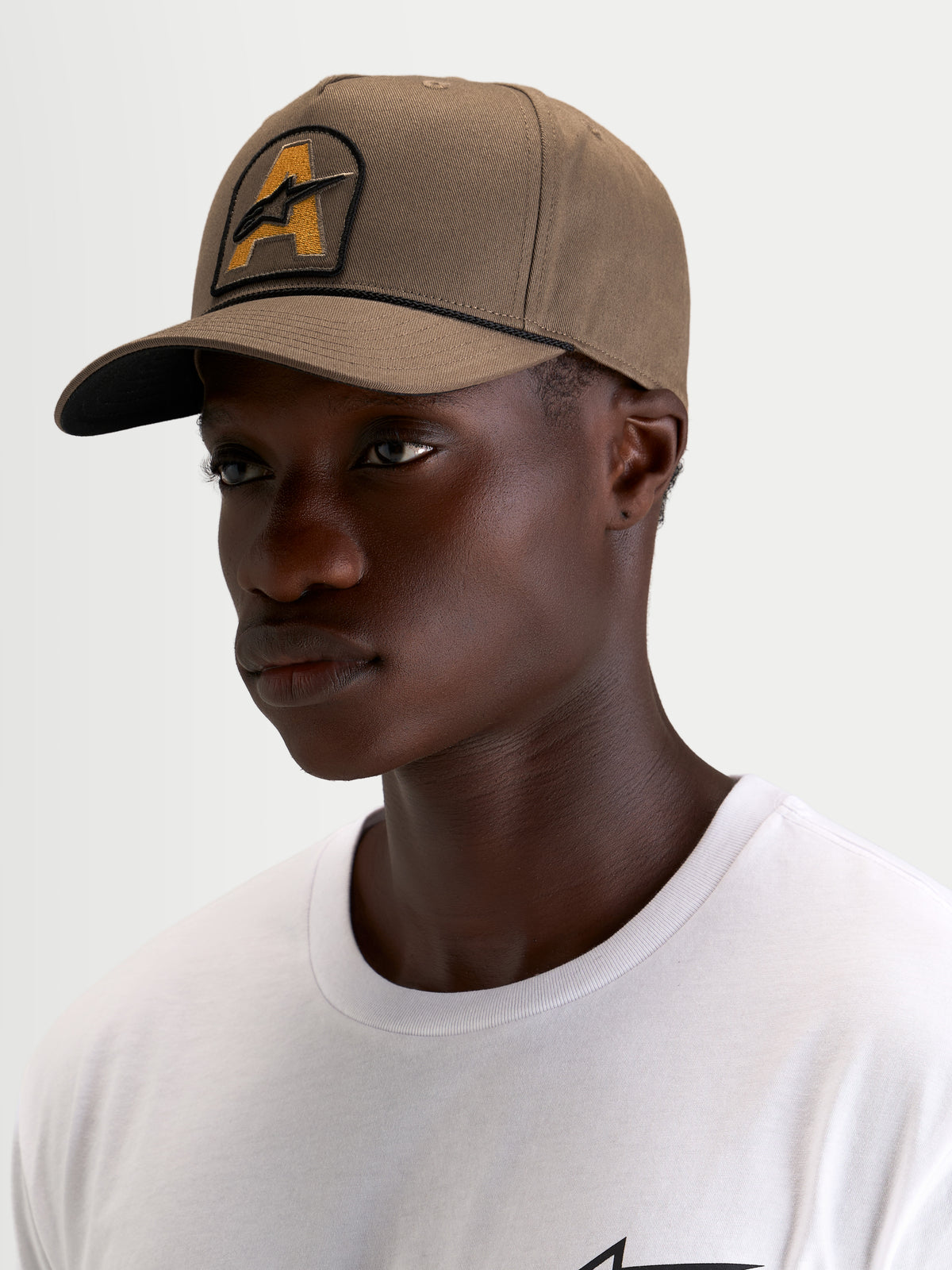 Alpinestars Acme Snapback keps, brun vardagskeps med böjd skärm, strukturerad krona och broderad Astars-logotyp framtill med repkant, bars av en modell