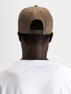 Alpinestars Acme Snapback keps, brun vardagskeps i sportswear-stil, bärs bakofram av en modell, med justerbar snapback-stängning och bakre logotypmärke