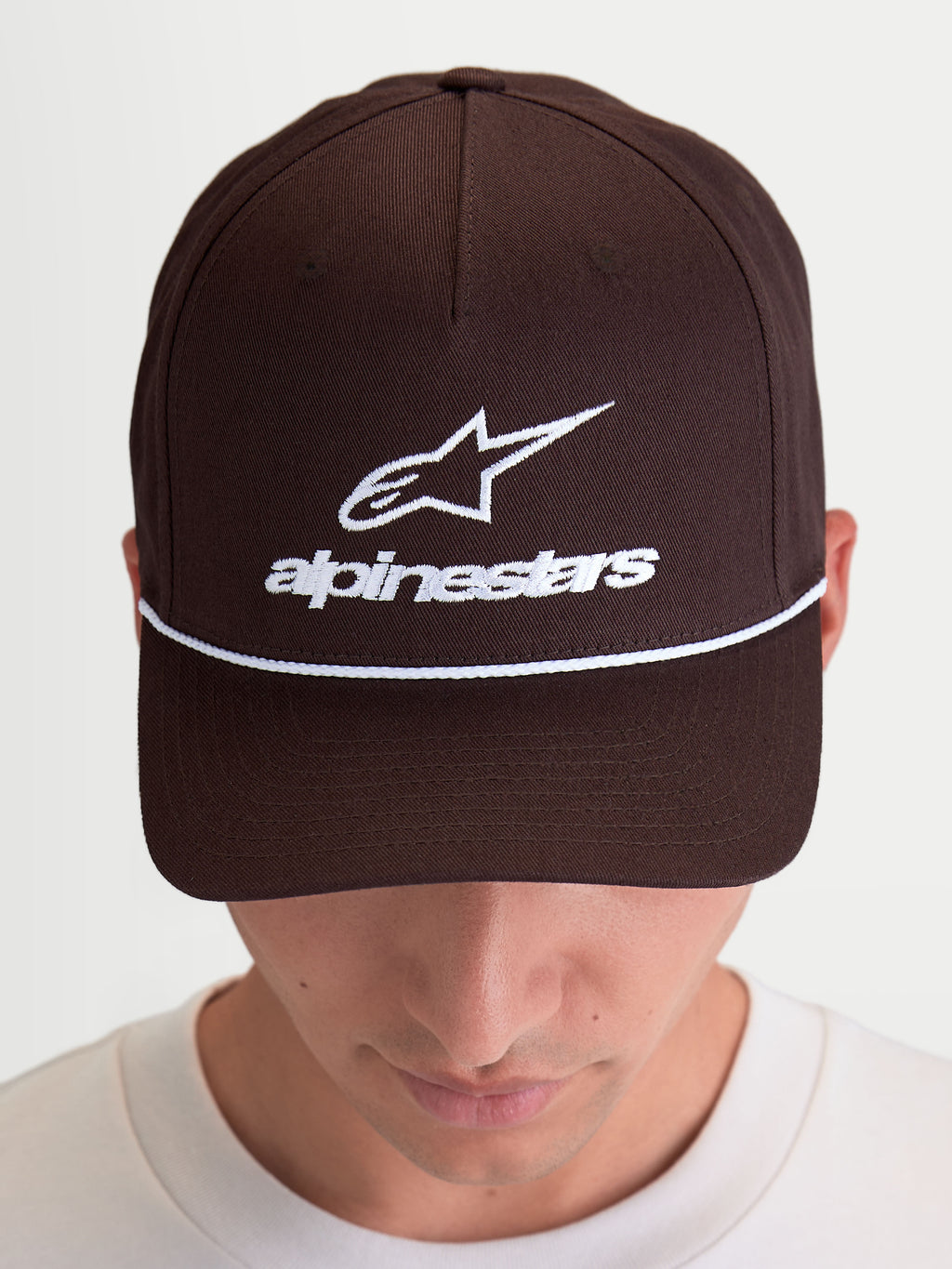 Alpinestars Combo Logo Snapback keps, brun motorsport-inspirerad keps med vit broderad logotyp och ordmärke framtill, böjd skärm, strukturerad krona och snapback-stängning, tillverkad i bomullstwill, visas på modell.