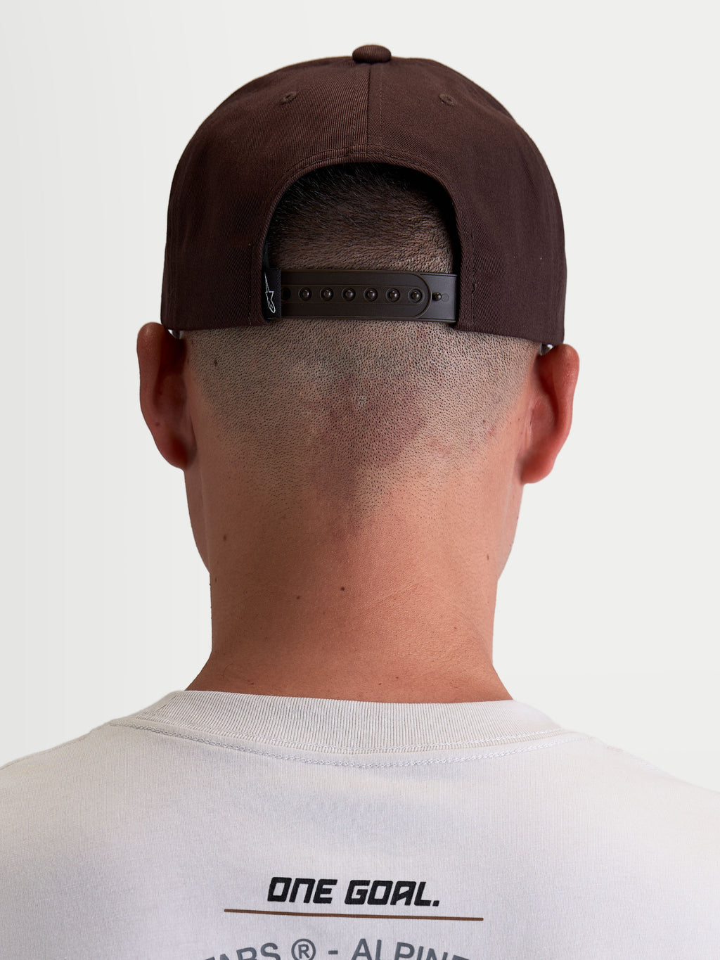 Alpinestars Combo Logo snapback keps, brun motorsportskeps i slitstark twill, vy bakifrån på modell som visar justerbar snapback-stängning och märkesetikett.