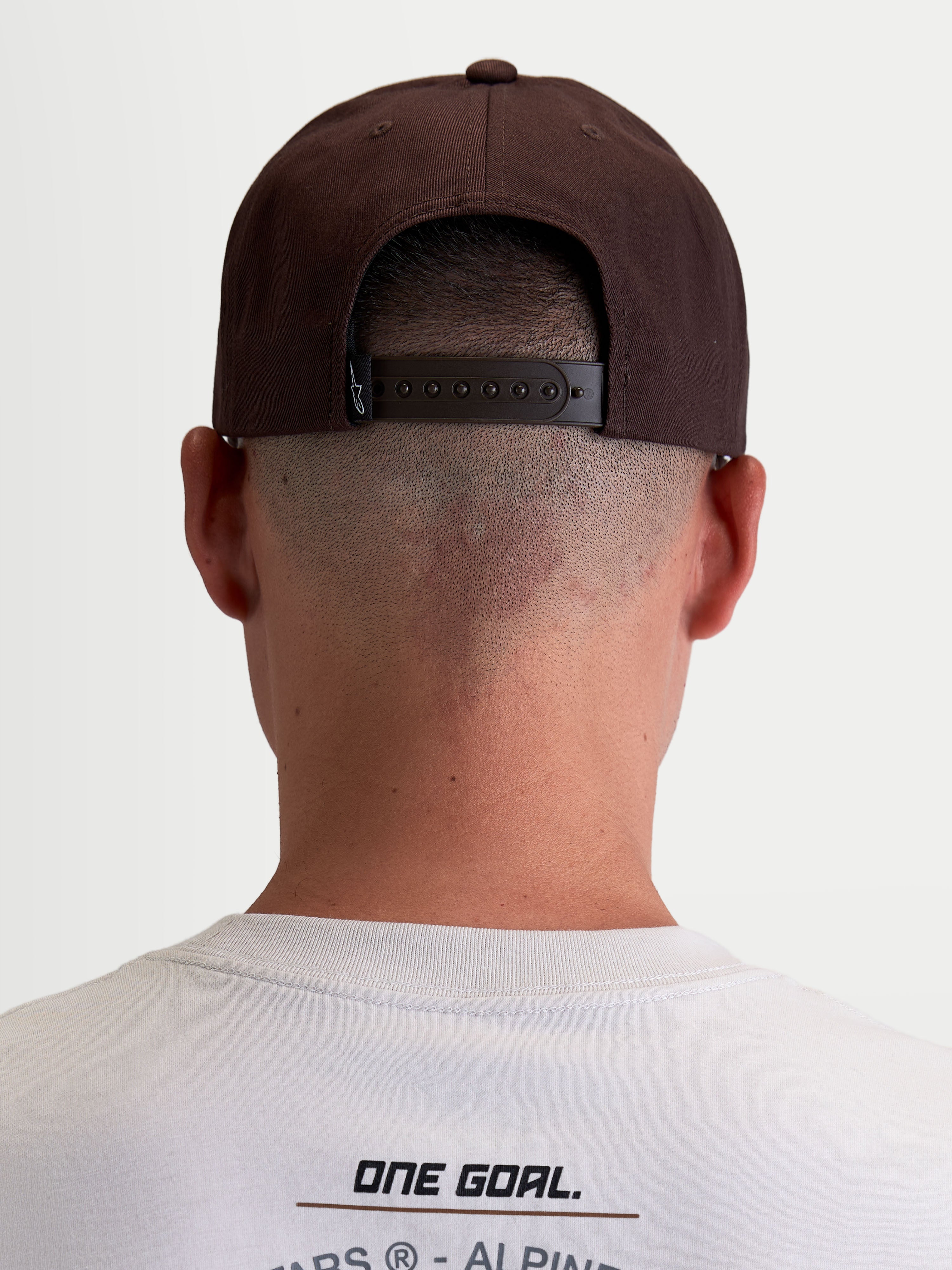 Alpinestars Combo Logo snapback keps, brun motorsportskeps i slitstark twill, vy bakifrån på modell som visar justerbar snapback-stängning och märkesetikett.