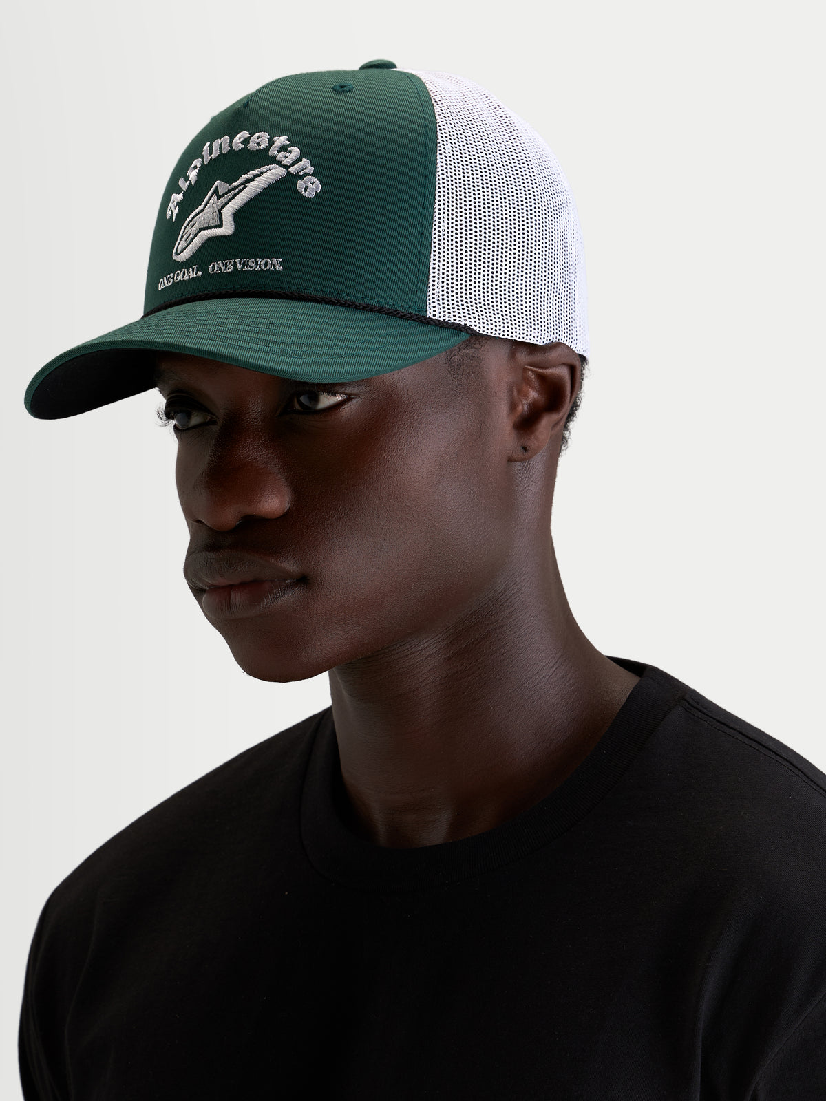 Alpinestars Baron Trucker Hat, casual sportswear cap worn by a model, green and white, featuring a curved bill, structured twill crown, breathable mesh back, and embroidered front logo