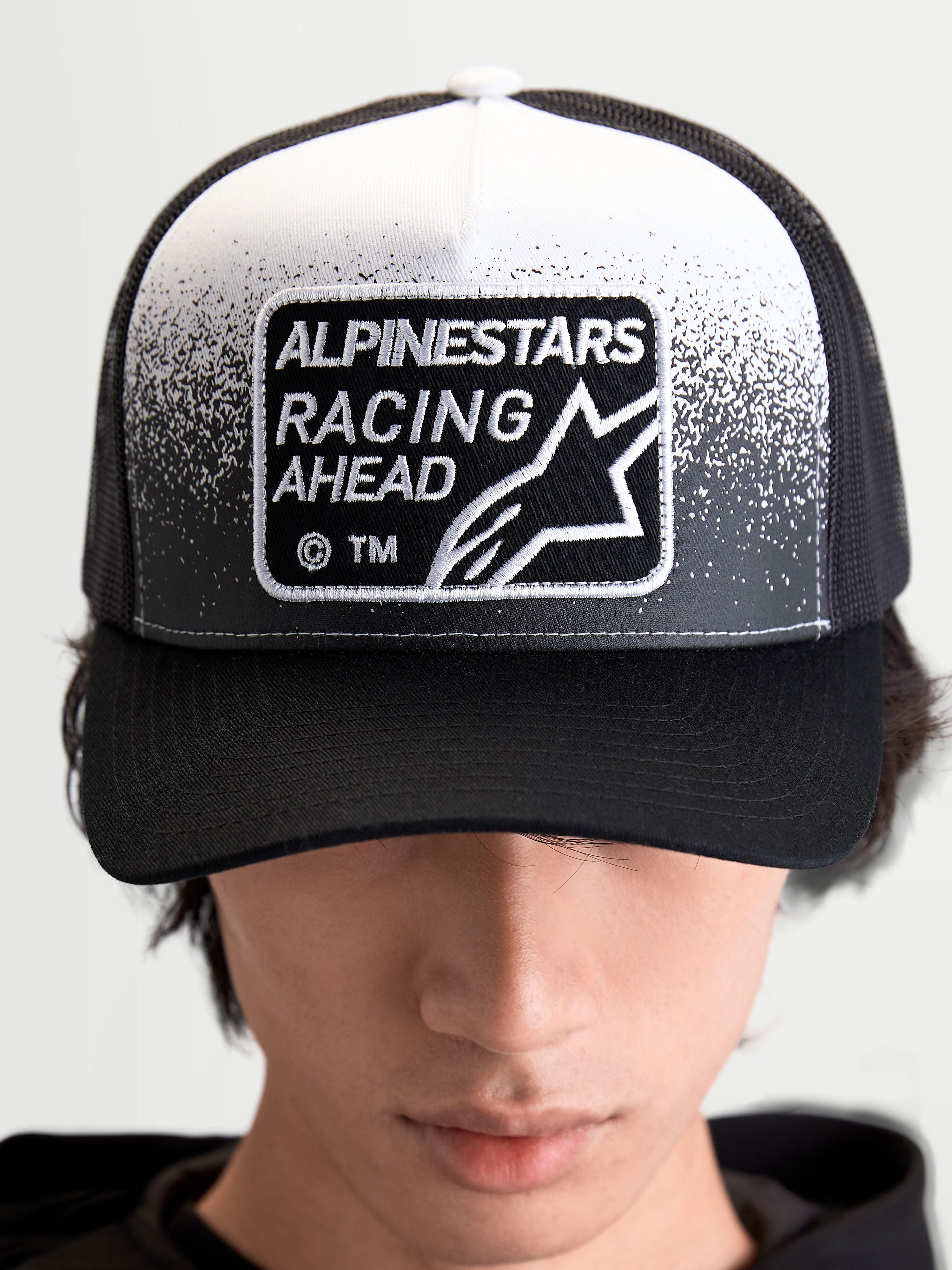 Alpinestars Gravel keps, svart och vit truckerkeps för både herr och dam, med en vävd Alpinestars Racing Ahead-patch, strukturerad krona och böjd skärm, frontvy på modell.