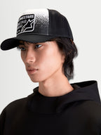 Alpinestars Gravel keps, trucker-keps för vardagsbruk på modell, svart och vit, med strukturerad krona, böjd skärm, ventilerande mesh-baksida och vävd patch med grustexturerad grafik och Alpinestars Racing Ahead-branding.