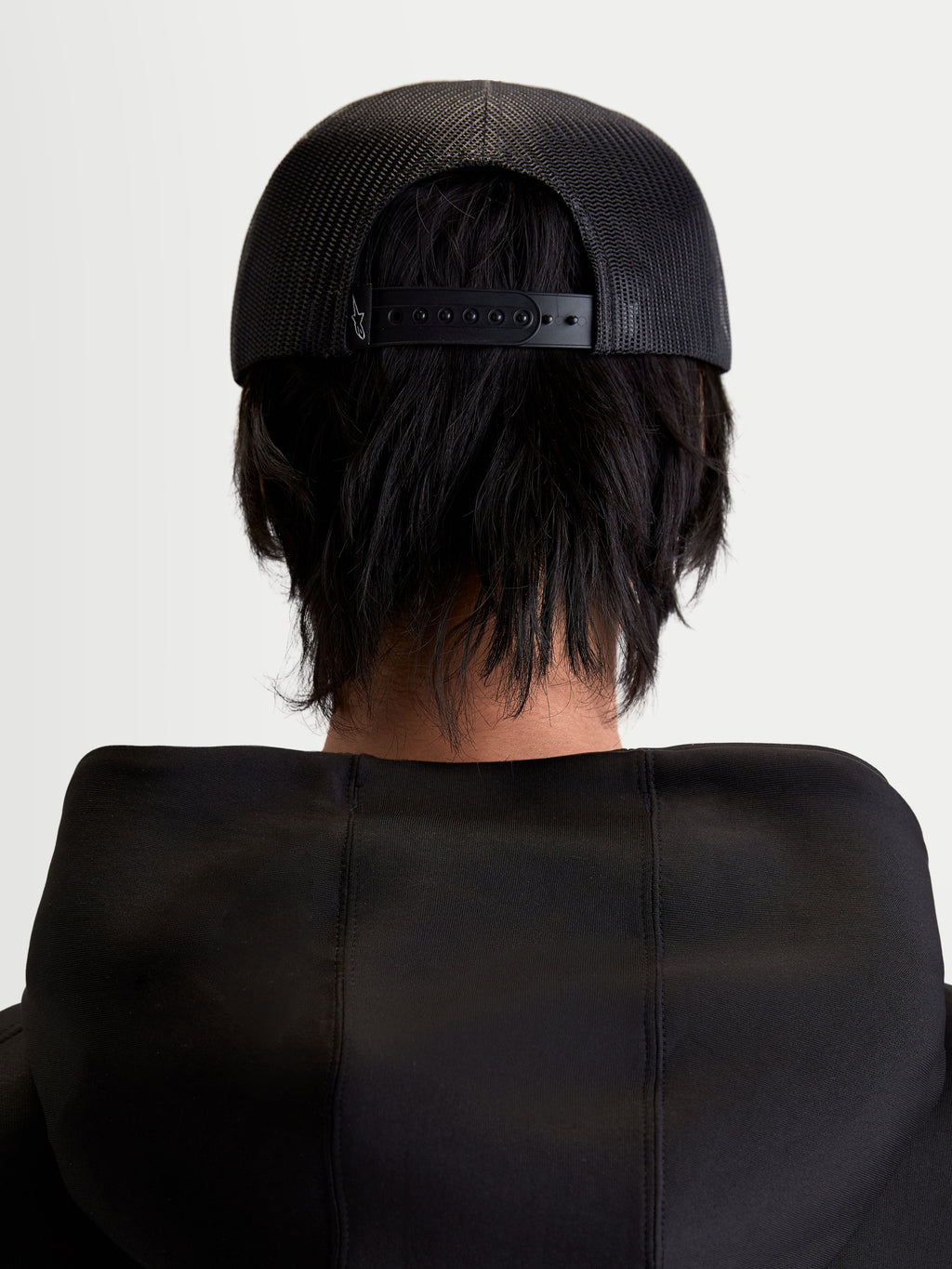 Alpinestars Gravel keps, svart snapback-keps i unisex-modell, sedd bakifrån på en modell som visar den andningsbara baksidan i mesh och justerbart snäppspänne.