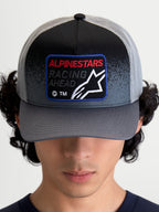 Alpinestars Gravel keps, mörkgrå och svart keps i truckermodell med böjd skärm och vävd frontpatch med texten Racing Ahead och Astars-logotyp, frontvy på modell.