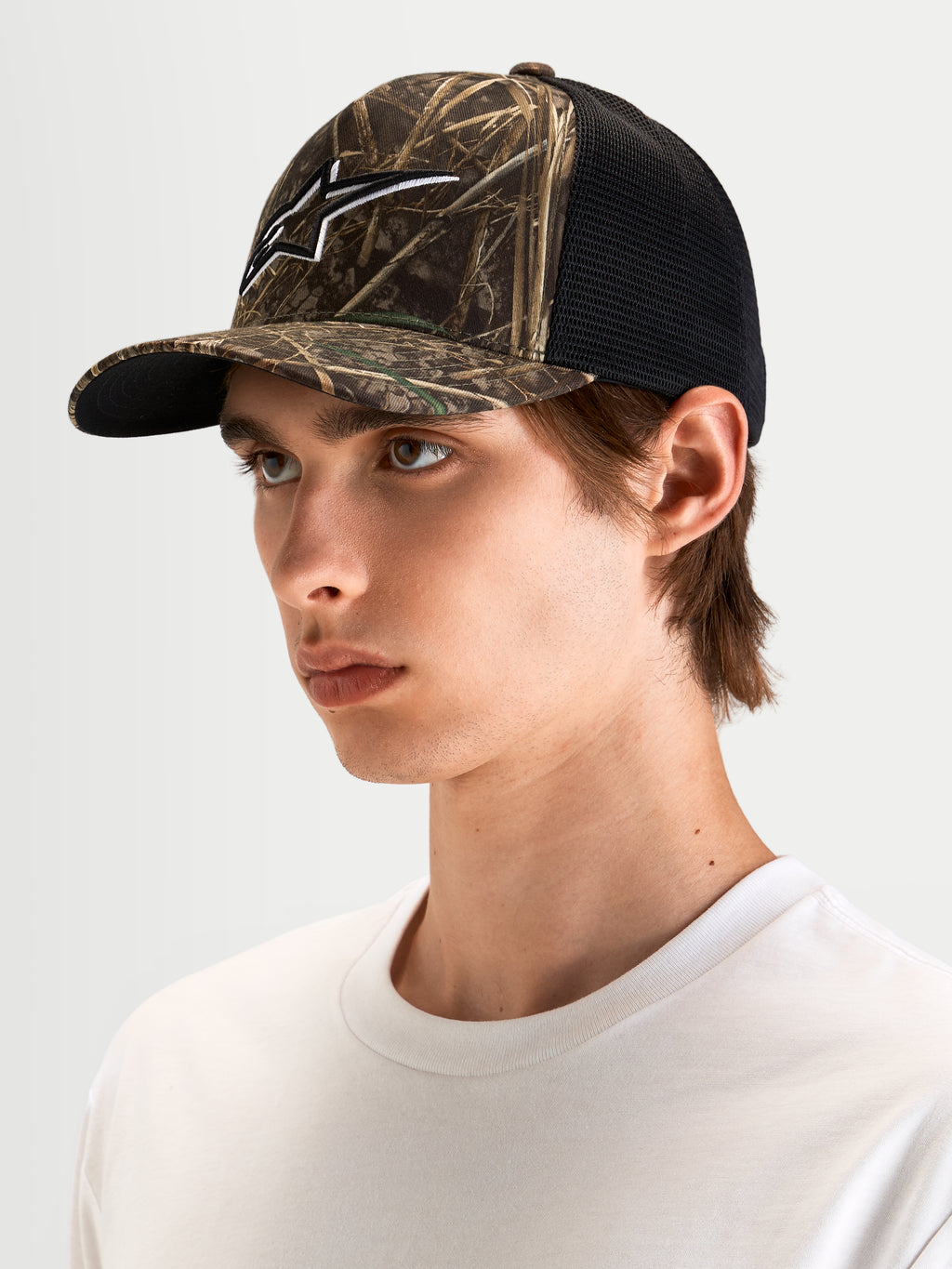 Alpinestars Thicket Realtree Trucker Hat, sportswear trucker cap in Realtree camo and black, curved bill, structured crown, and 3D embroidered Astars logo, worn by a model.