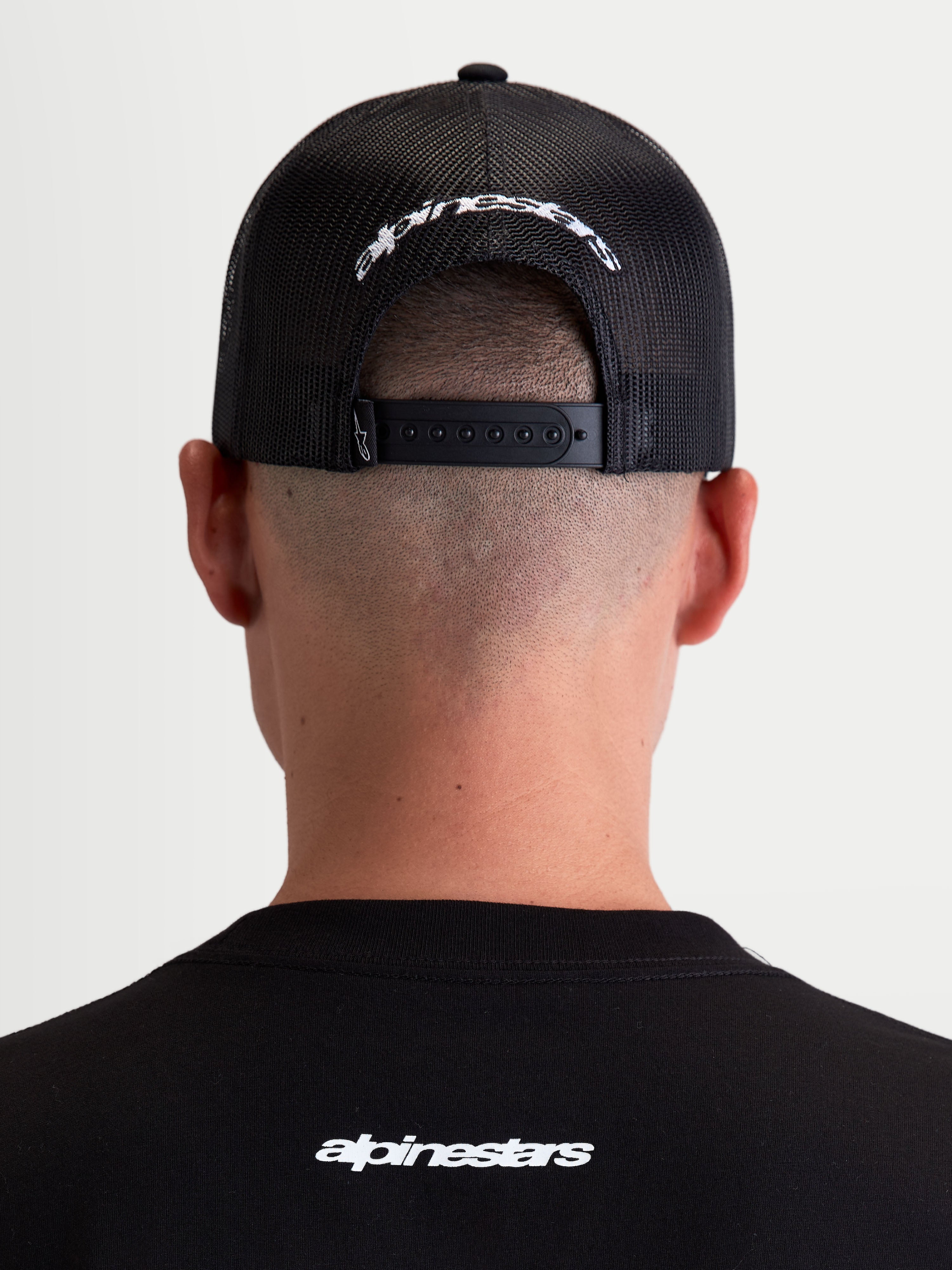 Alpinestars Meteorite keps, svart och vit truckerkeps med nätbaksida sedd bakifrån på modell, justerbar snapback-stängning och vit broderad Alpinestars-logotyp, sportig vardagskeps.