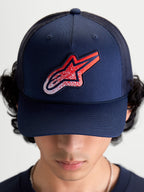 Alpinestars Meteorite keps, mörkblå trucker-keps för både dam och herr med röd och vit grustexturerad Astars-logotyp, strukturerad krona, böjd skärm och ventilerande mesh-baksida, visad framifrån på modell.