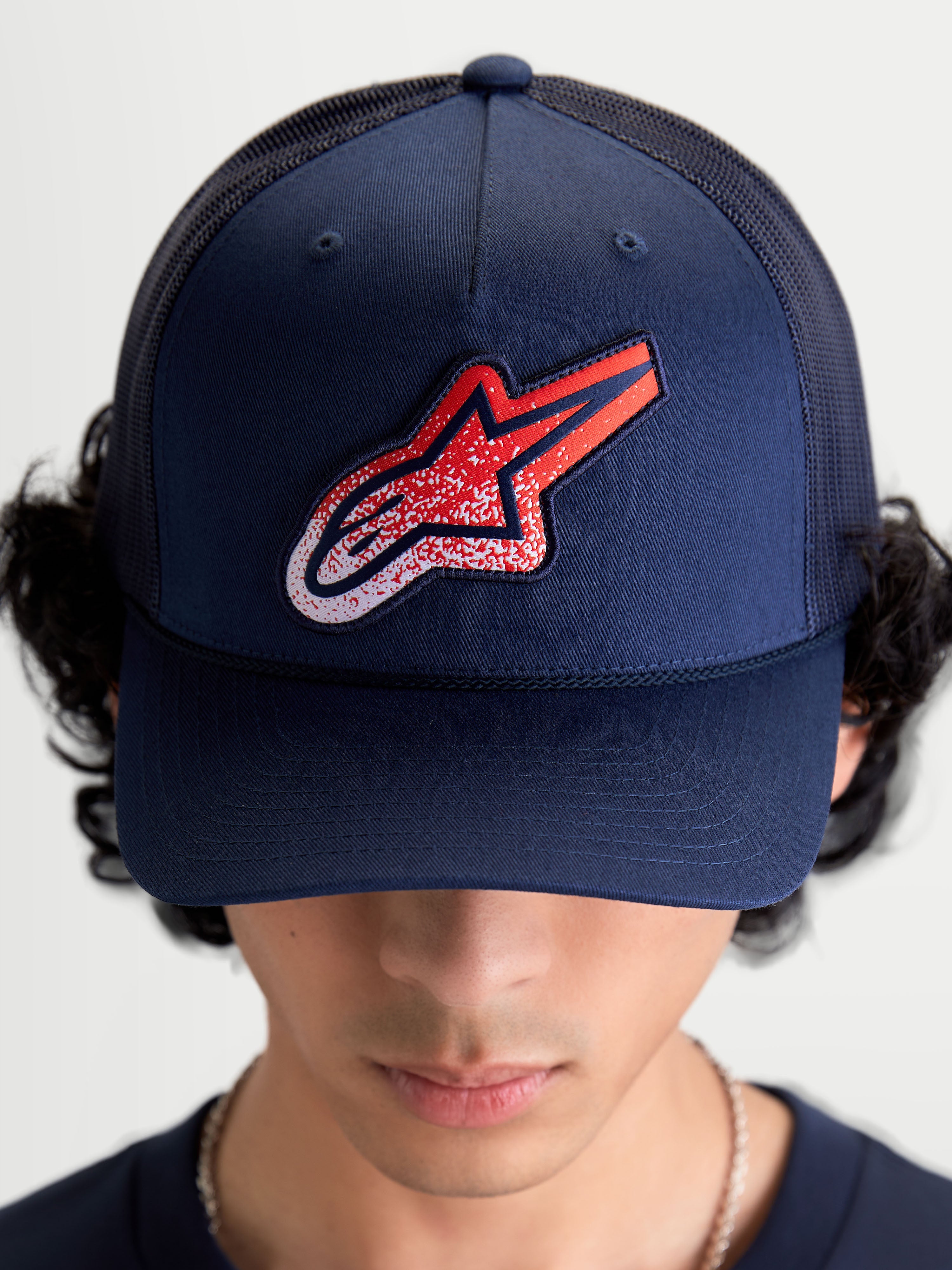 Alpinestars Meteorite keps, mörkblå trucker-keps för både dam och herr med röd och vit grustexturerad Astars-logotyp, strukturerad krona, böjd skärm och ventilerande mesh-baksida, visad framifrån på modell.