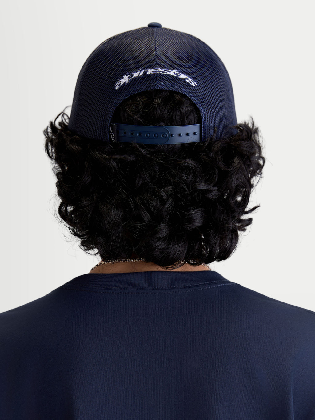 Alpinestars Meteorite keps, mörkblå truckerkeps sedd bakifrån på modell, ventilerande mesh-paneler baktill, justerbar snapback-stängning och vit broderad Alpinestars-logotyp, sportigt huvudplagg för vardagsbruk