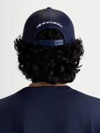 Alpinestars Meteorite keps, mörkblå truckerkeps sedd bakifrån på modell, ventilerande mesh-paneler baktill, justerbar snapback-stängning och vit broderad Alpinestars-logotyp, sportigt huvudplagg för vardagsbruk