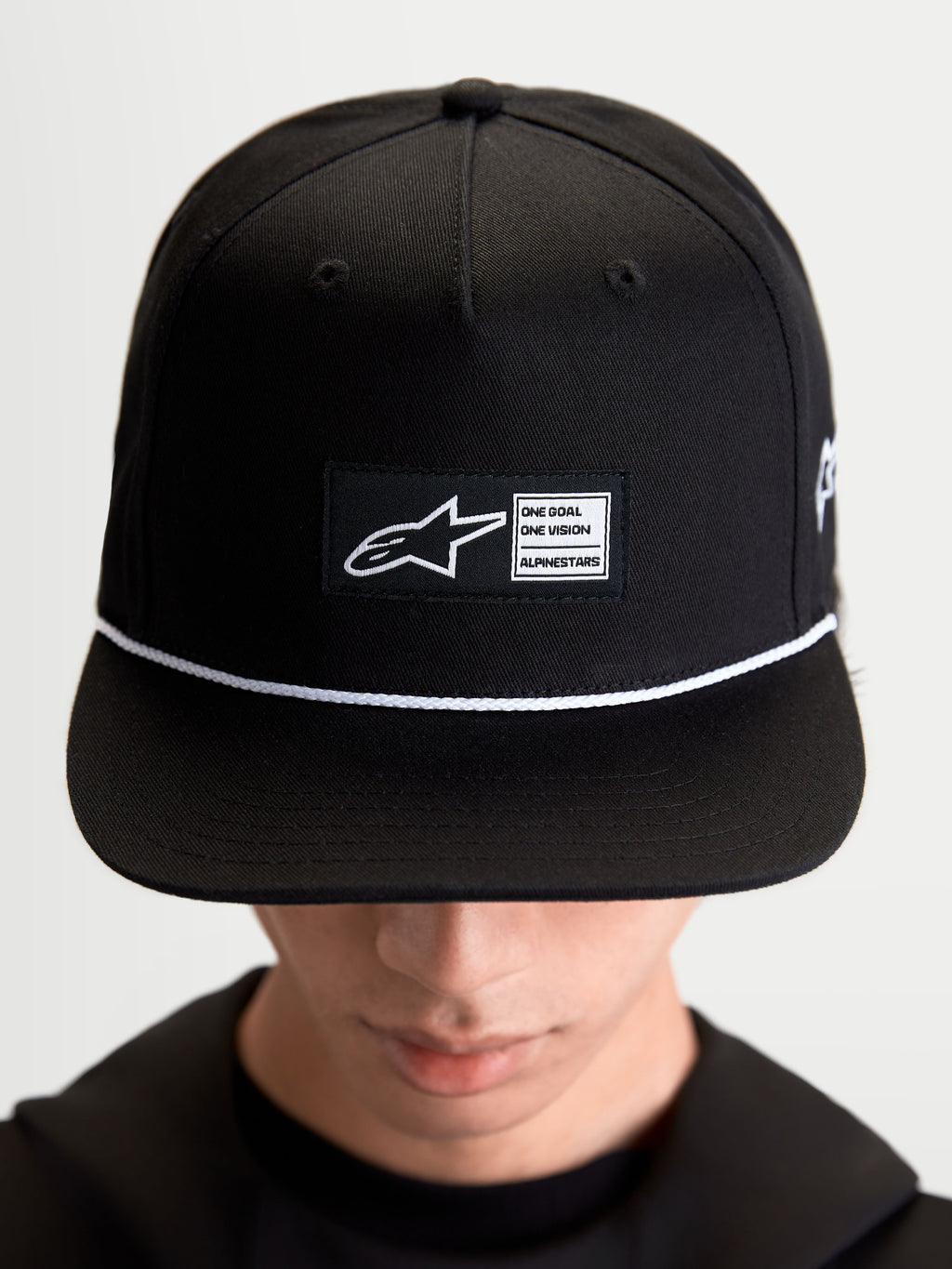 Alpinestars Label snapback-keps, svart och vit livsstilskeps i bomullstwill, strukturerad krona med platt skärm, vit snördetalj och vävd logotyplapp fram med Alpinestars-märkning, visad på modell.
