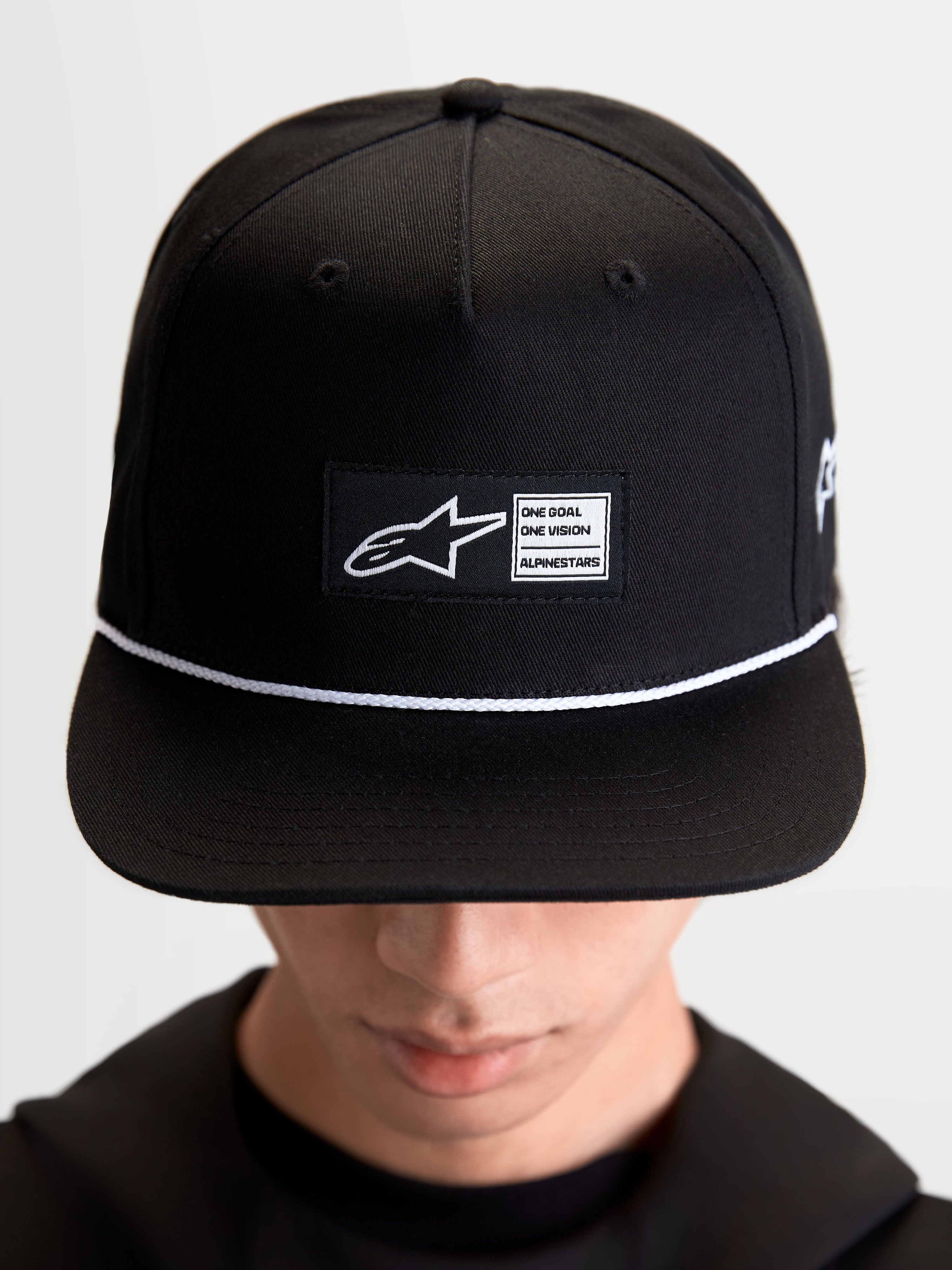 Alpinestars Label snapback-keps, svart och vit livsstilskeps i bomullstwill, strukturerad krona med platt skärm, vit snördetalj och vävd logotyplapp fram med Alpinestars-märkning, visad på modell.