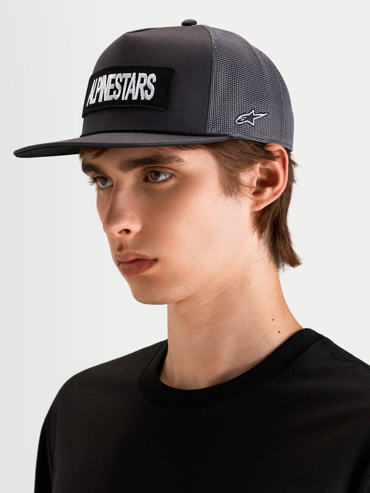 Alpinestars Ten trucker-keps, platt skärm, mörkgrå, båras av modell, med broderad Alpinestars logotyppatch framtill och Astars-brodyr på sidan
