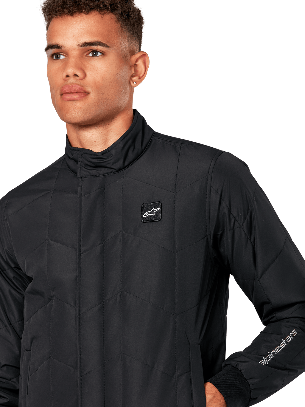 Alpinestars Precedent Jacka, quiltad sportjacka för herr i svart, närbild som visar den låga ståkragen, logomärke på bröstet och broderi på ärmen, med ett ikoniskt vinklat quiltmönster för en motorsport-inspirerad look.