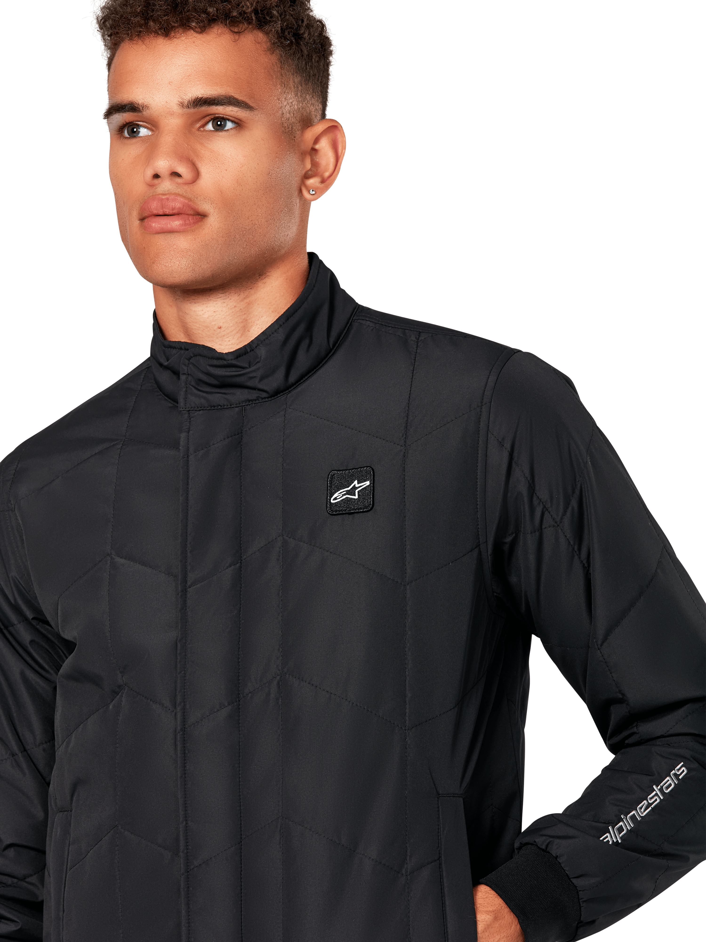 Alpinestars Precedent Jacka, quiltad sportjacka för herr i svart, närbild som visar den låga ståkragen, logomärke på bröstet och broderi på ärmen, med ett ikoniskt vinklat quiltmönster för en motorsport-inspirerad look.