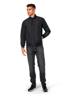 Alpinestars Precedent Jacket, quiltad sportjacka, svart, bärs med mörkgrå jeans och svarta sneakers, med ett vinklat quiltmönster, låg ståkrage, ribbstickade muddar och nederkant, vitt logomärke på bröstet och broderi på ärmen.