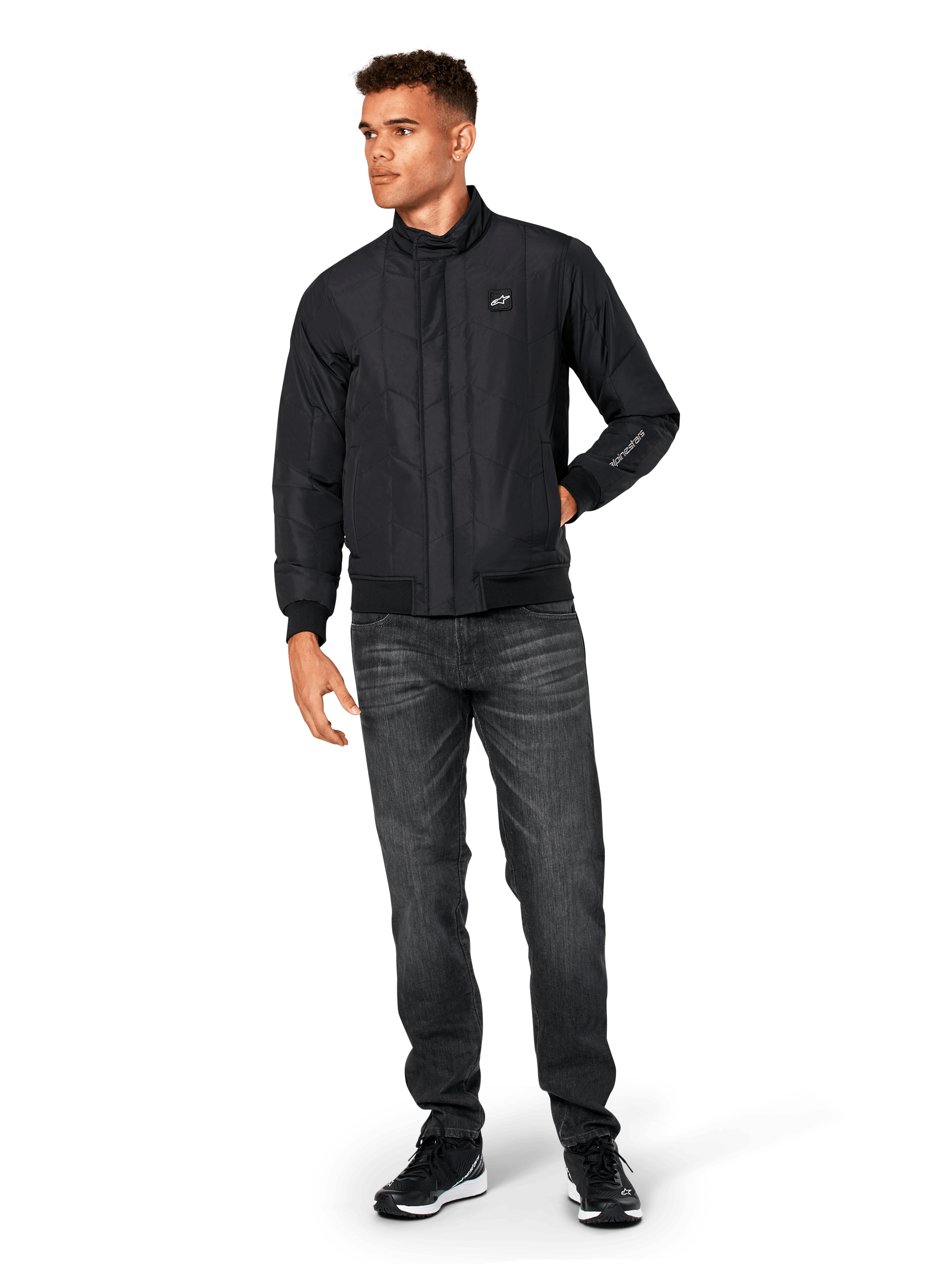 Alpinestars Precedent Jacket, quiltad sportjacka, svart, bärs med mörkgrå jeans och svarta sneakers, med ett vinklat quiltmönster, låg ståkrage, ribbstickade muddar och nederkant, vitt logomärke på bröstet och broderi på ärmen.