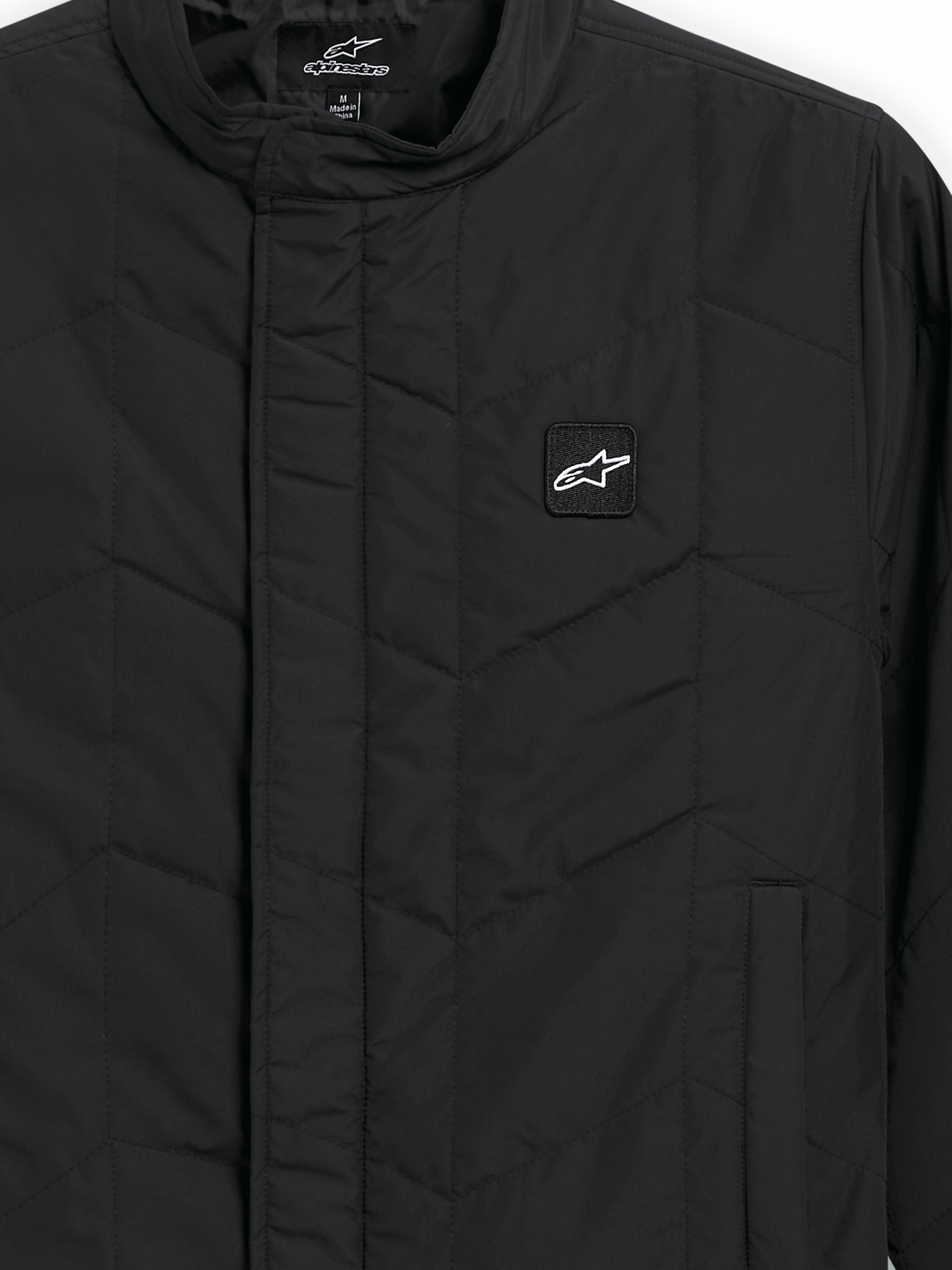 Alpinestars Precedent Jacka, quiltad sportswearjacka, svart, närbild som visar ett ikoniskt vinklat quiltmönster, låg ståkrage, täckt dragkedja framtill och ett litet logomärke på bröstet