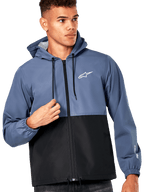 Manlig modell i Alpinestars Speeder vindjacka, blockfärgad design i skifferblått och svart, huva med svarta dragsnören, vit logotyp på bröstet, avslappnad motorsportinspirerad vindjacka