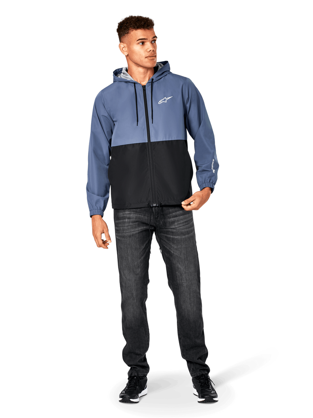Alpinestars Speeder vindjacka, skifferblå och svart, lättviktsjacka med huva och meshfoder, vit stjärnlogotyp på bröstet, bärs med svarta jeans och sneakers, vardaglig motorsport-streetwear-design