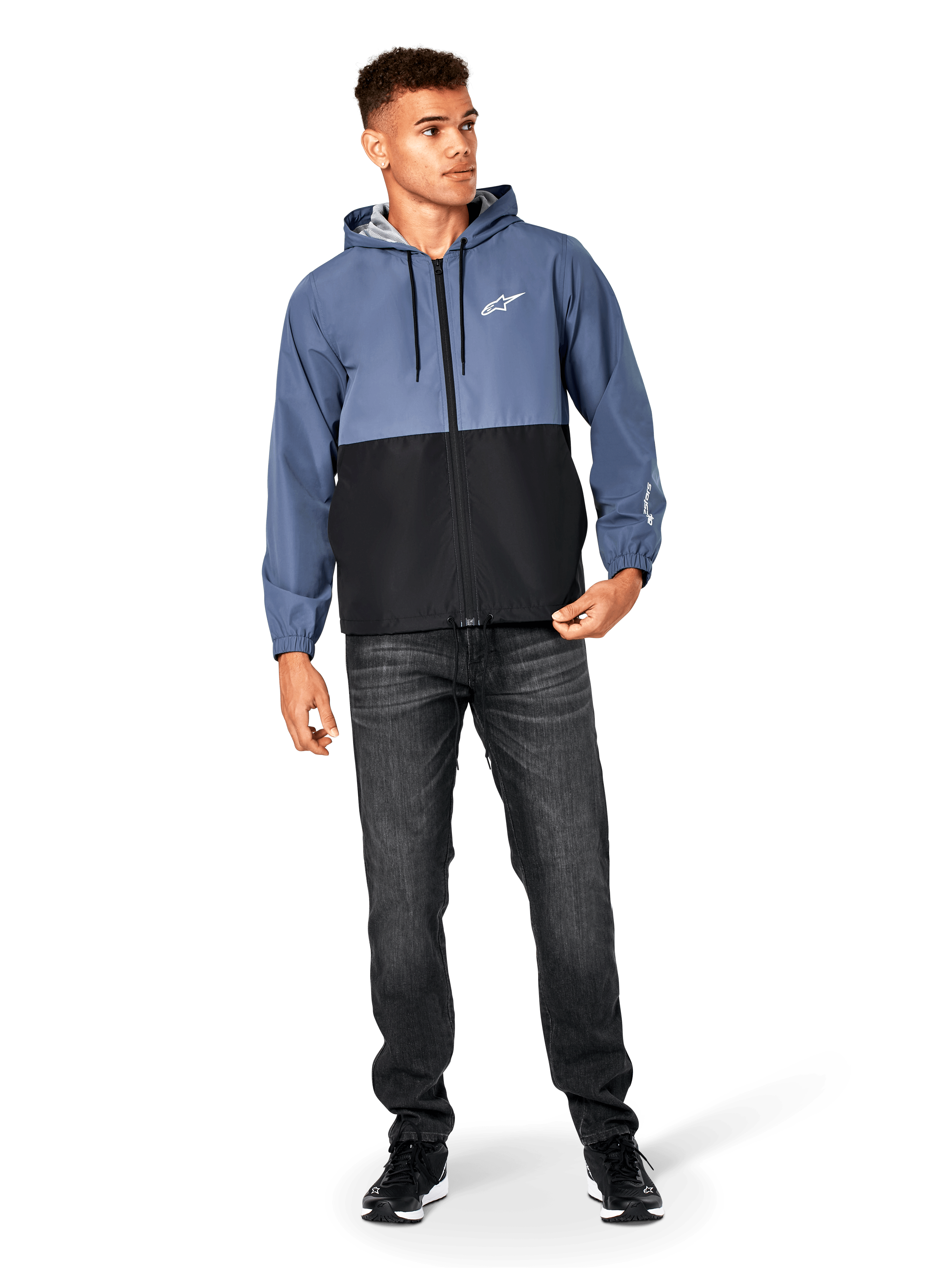 Alpinestars Speeder vindjacka, skifferblå och svart, lättviktsjacka med huva och meshfoder, vit stjärnlogotyp på bröstet, bärs med svarta jeans och sneakers, vardaglig motorsport-streetwear-design