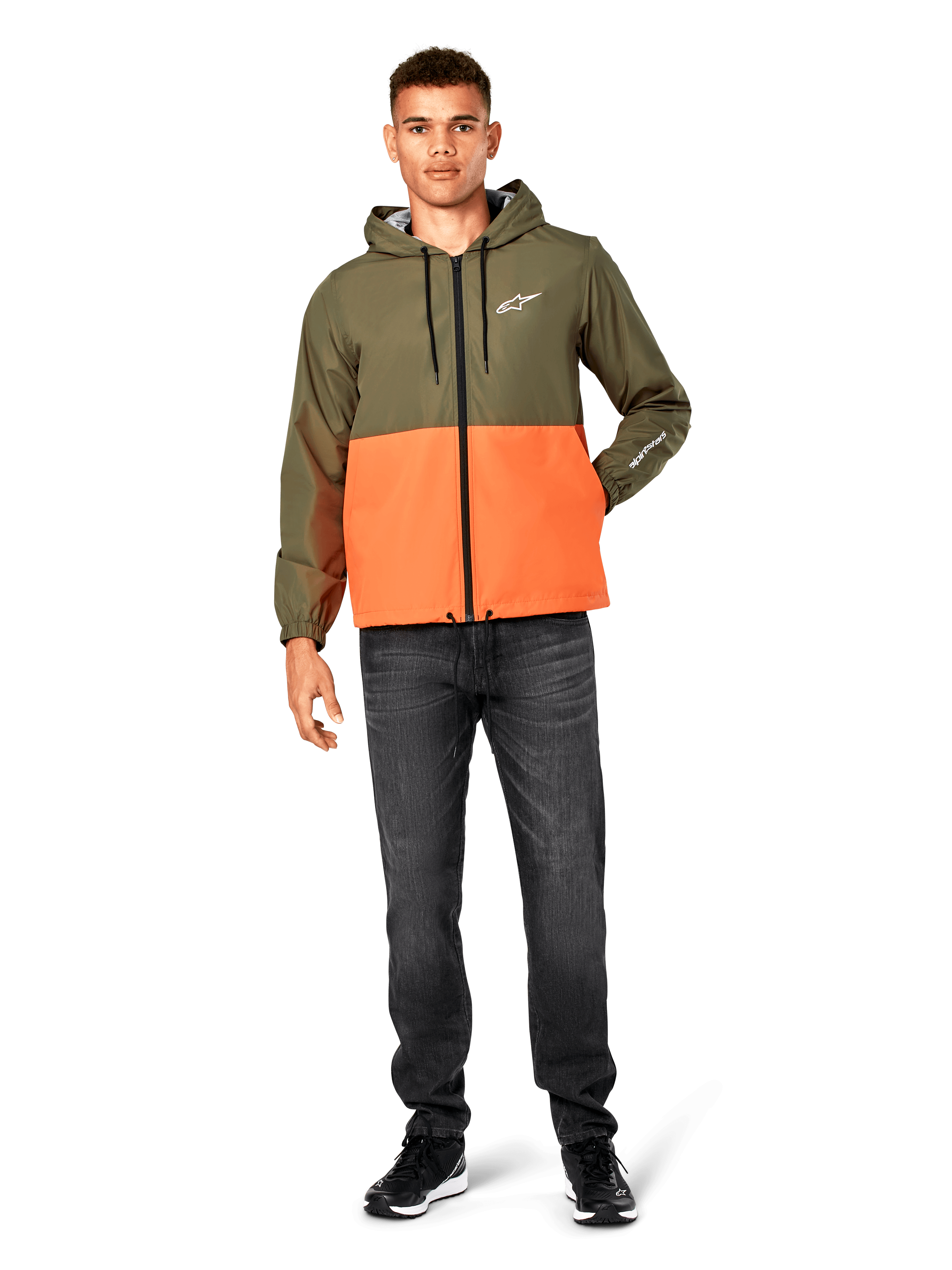 Alpinestars Speeder Windbreaker Jacket, blockfärgad i militärgrönt och orange, lätt jacka med huva, svarta dragsnören och dragkedja framtill, vit logotyp på bröstet och ärmen, bärs med mörka jeans och svarta sneakers, avslappnad sportstil.