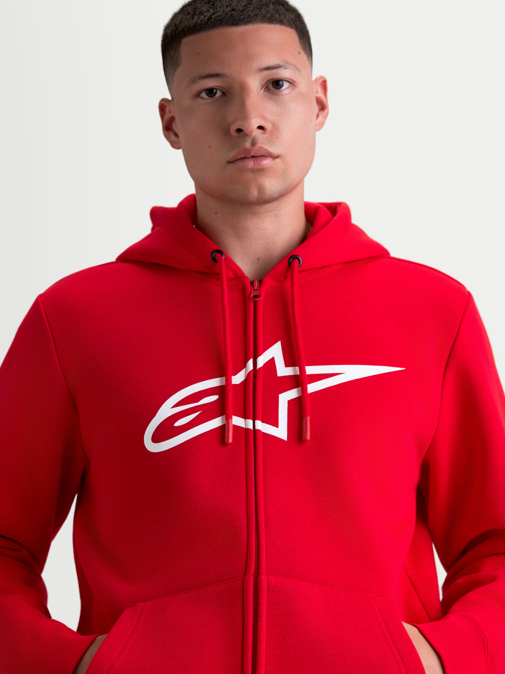 Alpinestars Ageless Zip V3 huvtröja, röd och vit sportswear-fleecehuvtröja med dragkedja, stor vit A-star-logotyp på bröstet, huva med justerbara dragskor och dold dragkedja framtill, motorsportinspirerad design på modell.