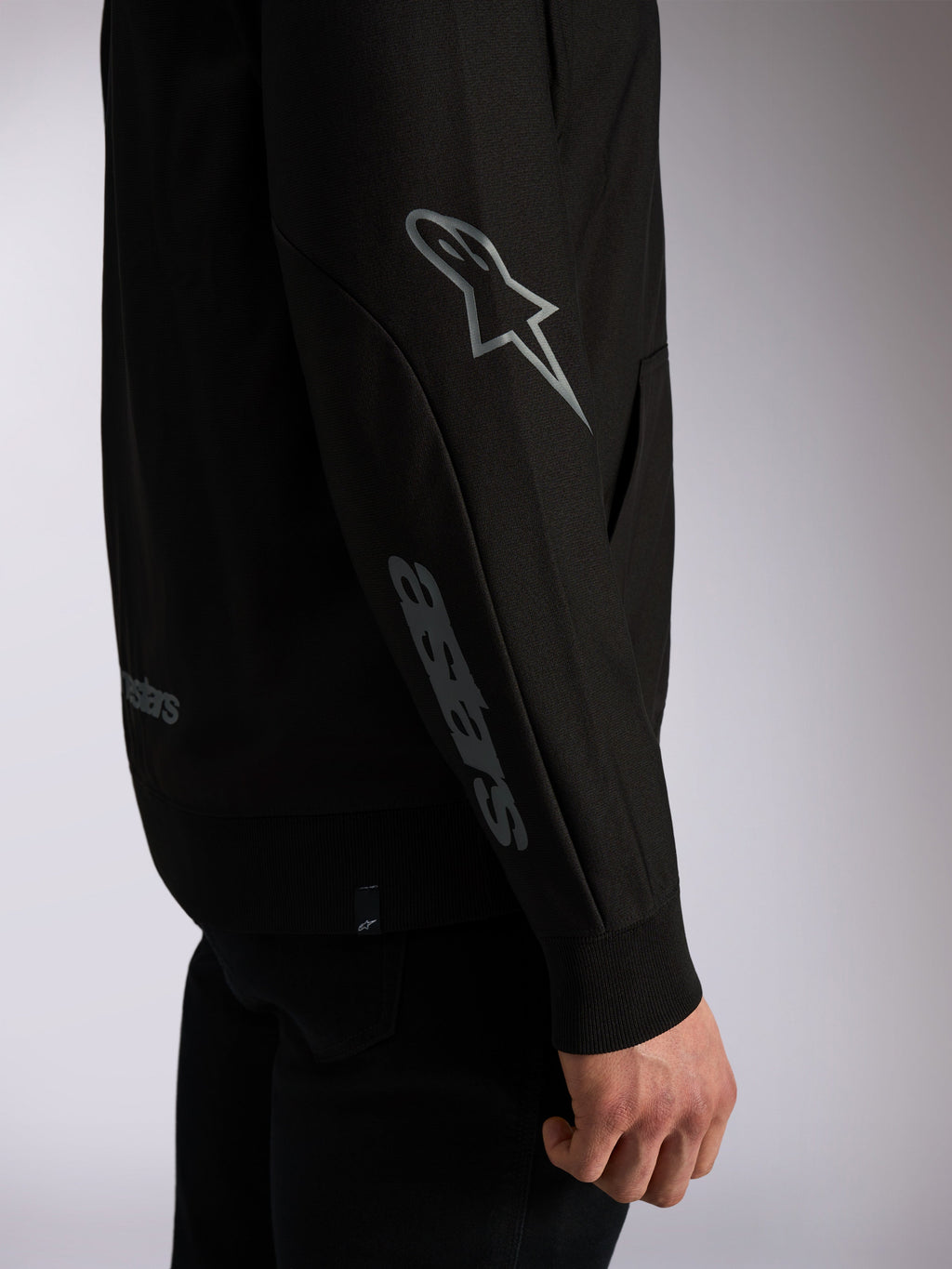 Alpinestars Sessions V3 Hoodie, black casual streetwear, close-up of sleeve featuring grey Astars logo on elbow and wordmark on forearm, ribbed cuffs, motorsport-inspired design