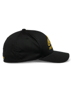 Alpinestars Gild Hat, sportswear-keps, svart och guld, sidoprofil med böjd skärm, strukturerad krona och guldmetalliskt 3D-broderi framtill och på sidan, stretch-twill-tyg