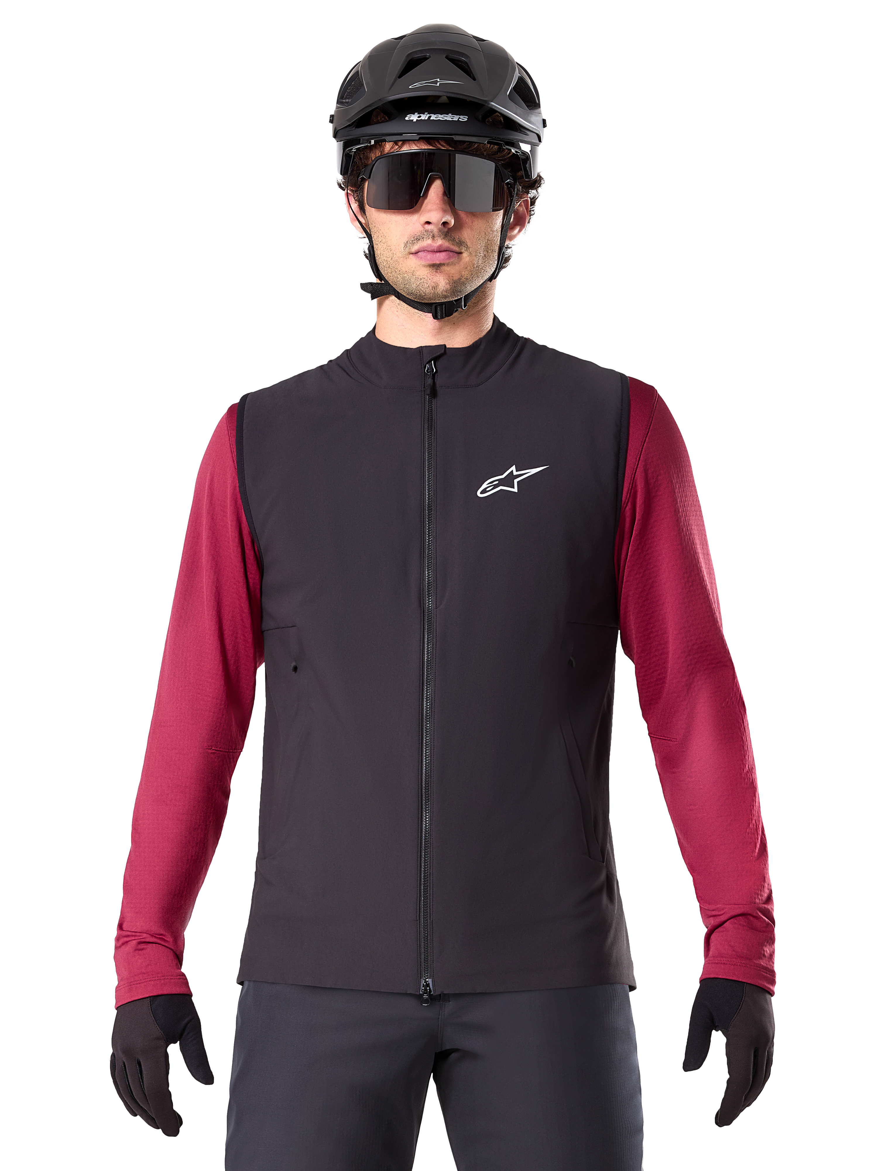 Alpinestars A-Dura Thermal Vest, svart isolerad cykelväst, bärs av en modell med en vinröd långärmad tröja, svart MTB-hjälm och solglasögon, med en vit logotyp på bröstet, lättviktigt termiskt skydd för mountainbike.