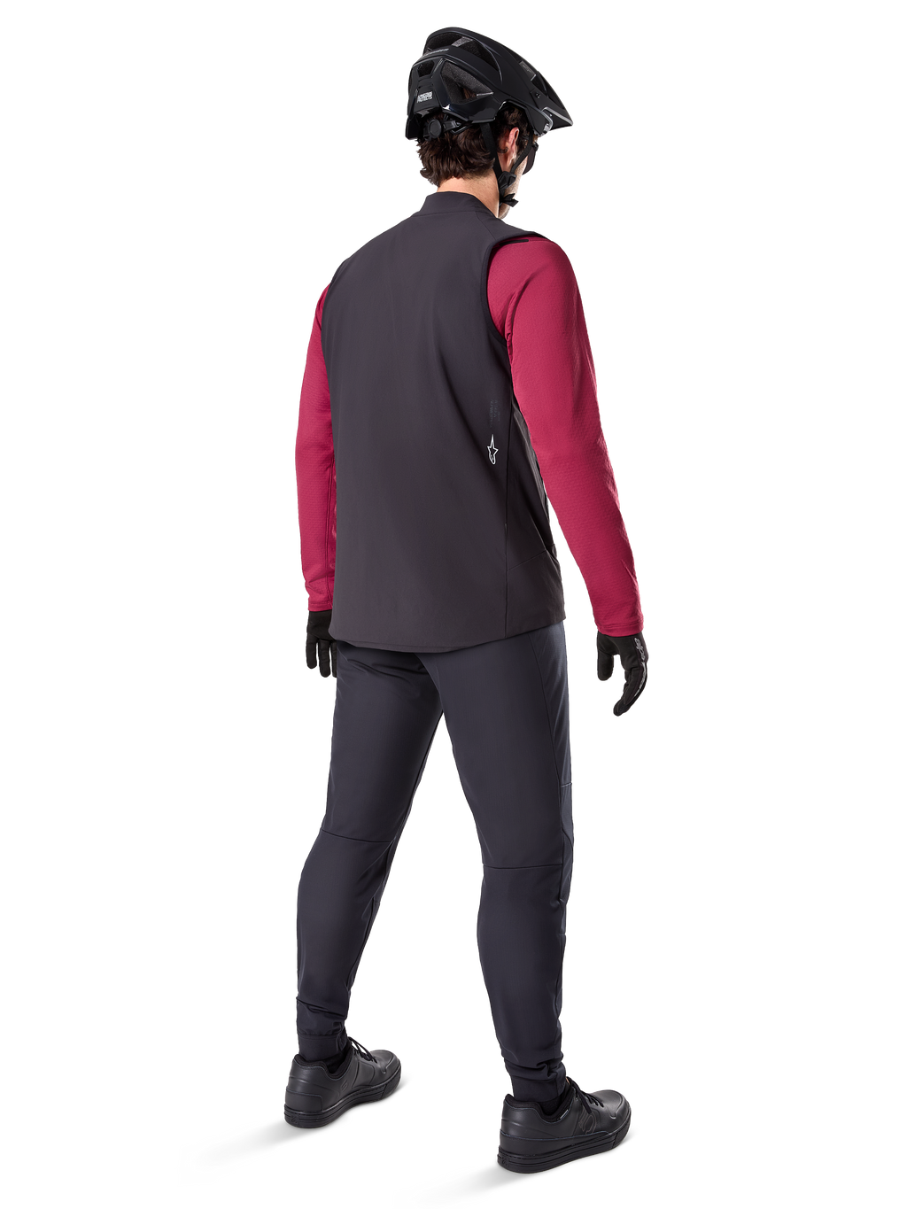 Alpinestars A-Dura Thermal Vest, svart cykelväst, sedd bakifrån på en modell som bär en vinröd långärmad tröja och svarta cykelbyxor, kombinerat med en svart mountainbikehjälm och handskar, teknisk utrustning för cykling i kallt väder