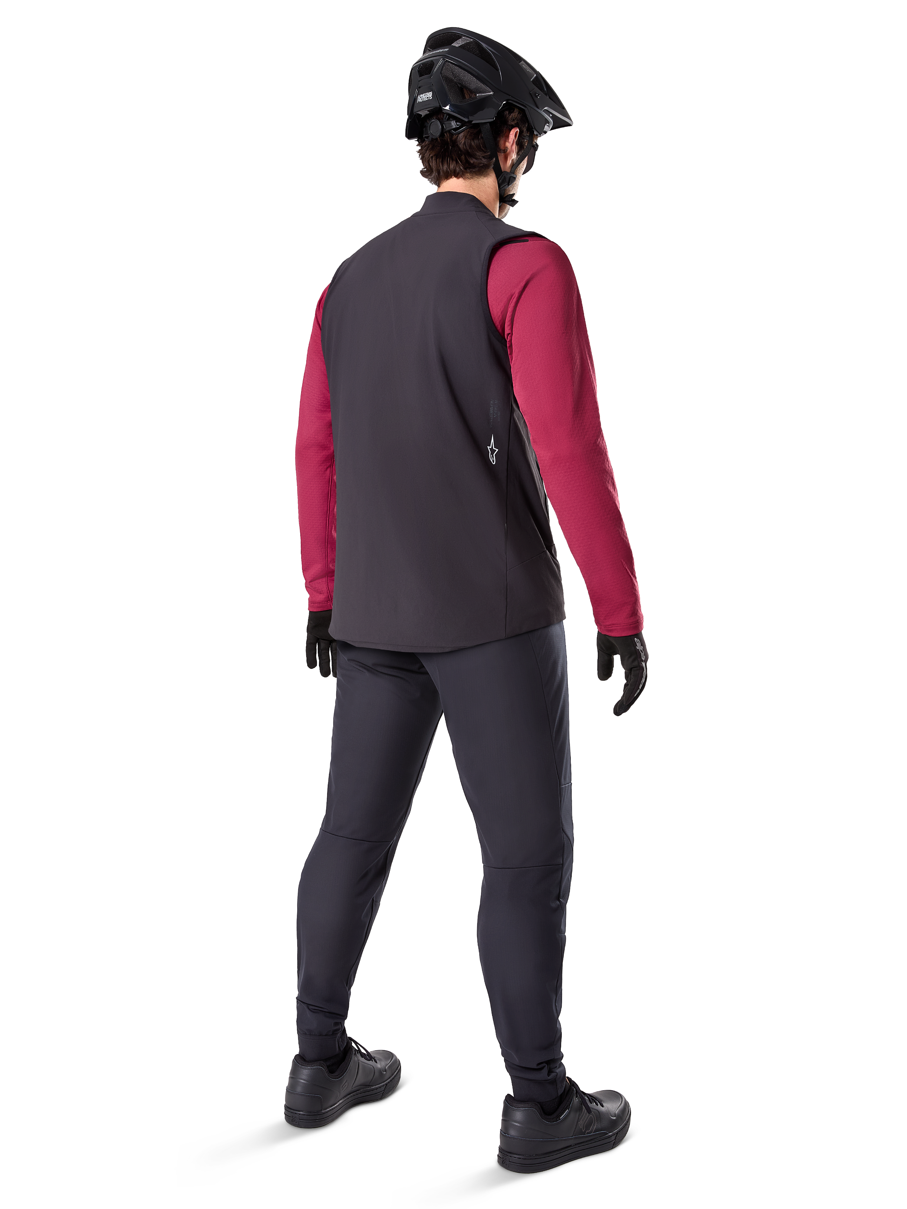 Alpinestars A-Dura Thermal Vest, svart cykelväst, sedd bakifrån på en modell som bär en vinröd långärmad tröja och svarta cykelbyxor, kombinerat med en svart mountainbikehjälm och handskar, teknisk utrustning för cykling i kallt väder
