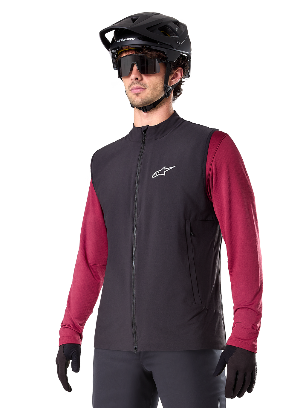 Alpinestars A-Dura Thermal Vest, svart, termisk cykelväst, bärs över en vinröd långärmad tröja, med en vit logotyp på bröstet, kombinerat med en svart MTB-hjälm och solglasögon, isolerande funktionslager för mountainbike