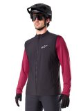 Alpinestars A-Dura Thermal Vest, svart, termisk cykelväst, bärs över en vinröd långärmad tröja, med en vit logotyp på bröstet, kombinerat med en svart MTB-hjälm och solglasögon, isolerande funktionslager för mountainbike
