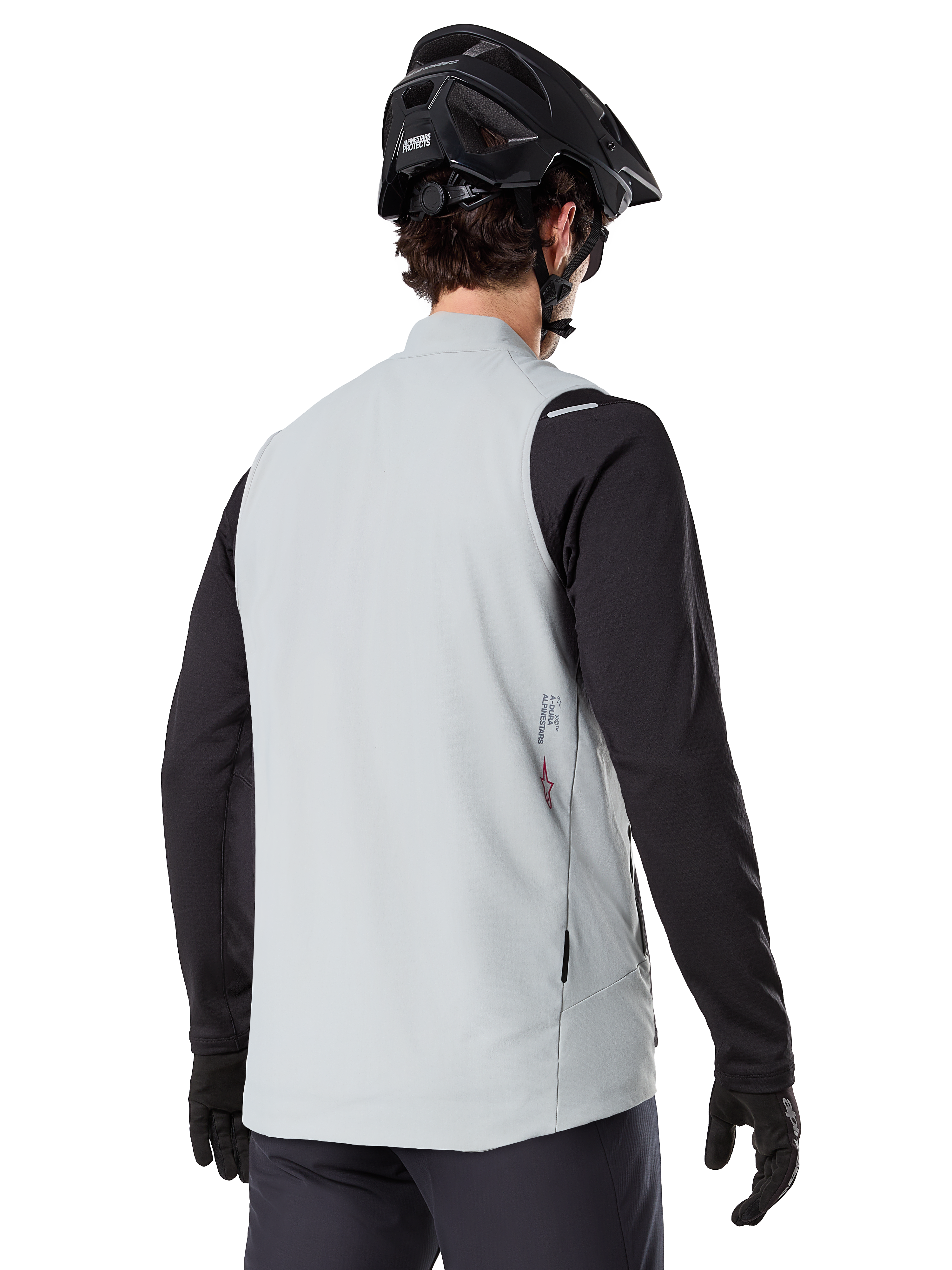 Alpinestars A-Dura termisk väst, titaniumgrå, bakifrån av modell som bär en svart långärmad tröja och MTB-hjälm, minimalistisk design med liten röd stjärnlogotyp på ryggen, lättisolerad cykelväst för terrängkörning