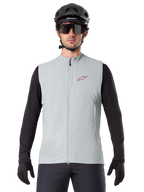 Alpinestars A-Dura Termisk Väst, cykelväst, titaniumgrå, bärs med en svart långärmad tröja och svart cykelhjälm, röd Alpinestars-stjärnlogotyp på bröstet, lätt och isolerad för mountainbikecykling