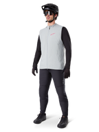Alpinestars A-Dura Thermal Vest, titaniumgrå cykelväst med rosa logotyp, bärs av en modell med svart långärmad tröja, mörkgrå byxor och svart mountainbikehjälm, funktionsutrustning för cykling i kallt väder