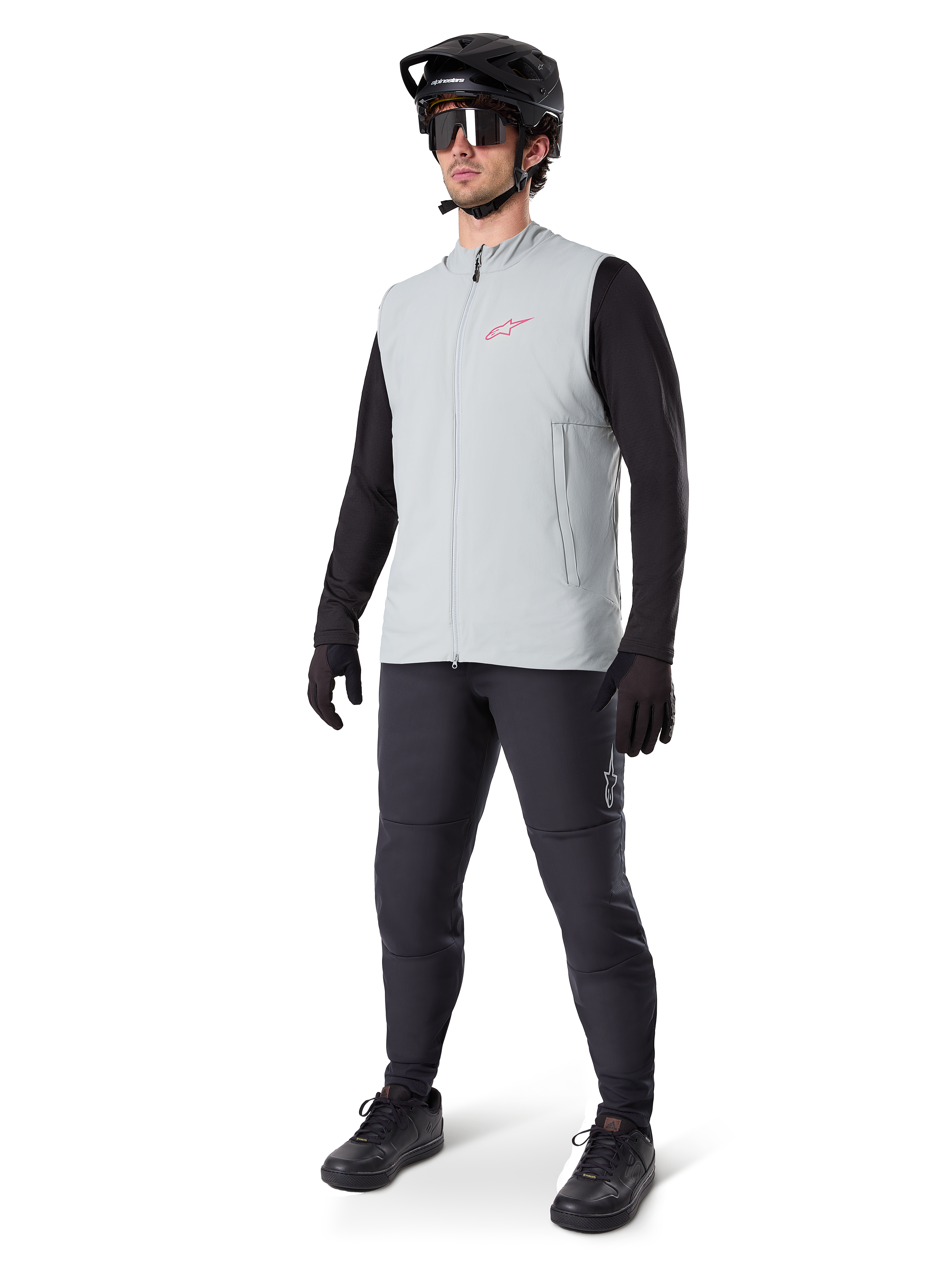 Alpinestars A-Dura Thermal Vest, titaniumgrå cykelväst med rosa logotyp, bärs av en modell med svart långärmad tröja, mörkgrå byxor och svart mountainbikehjälm, funktionsutrustning för cykling i kallt väder
