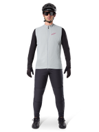 Alpinestars A-Dura Thermal Vest, cykelväst, Titanium Gray, bärs med svart långärmad tröja och svarta byxor, svart hjälm och solglasögon, röd Alpinestars-logotyp, lätt termisk isolering för mountainbike